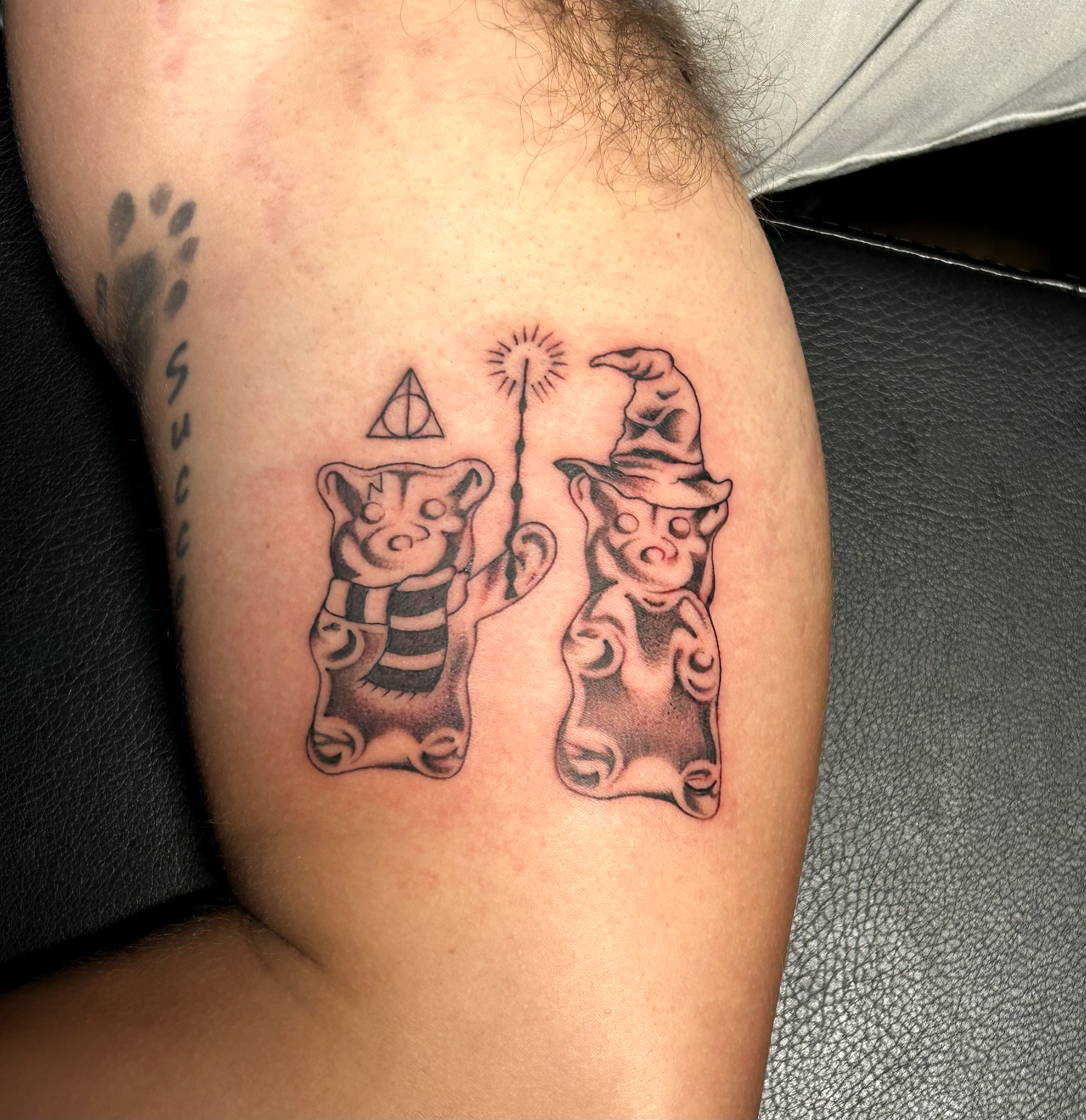 Tattoo of two teddy bears, one holding a wand with a star, and a triangle symbol above one bear, on a person's upper arm.