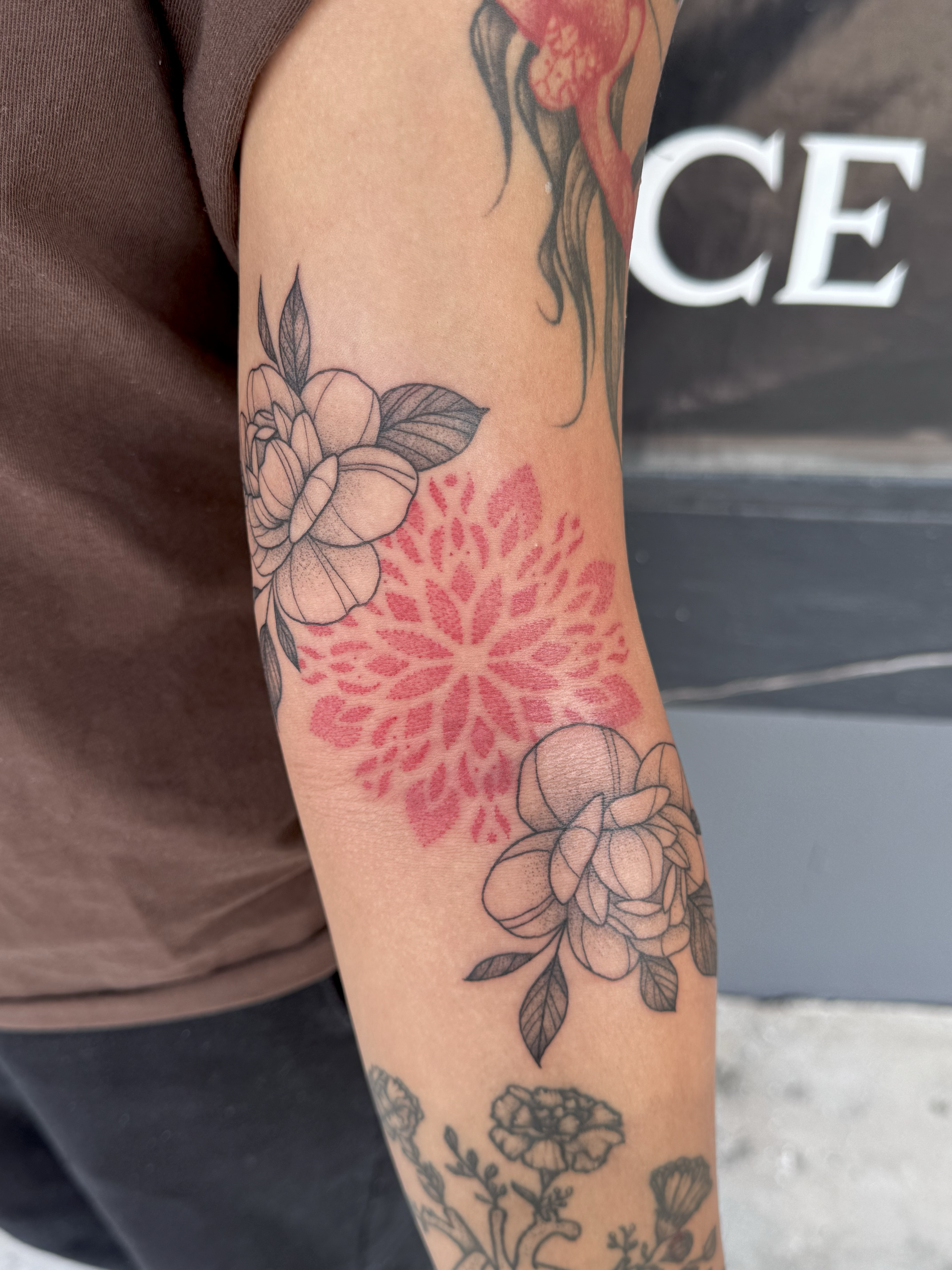 Tattooed arm with a pink floral design and black-and-gray flowers and leaves.