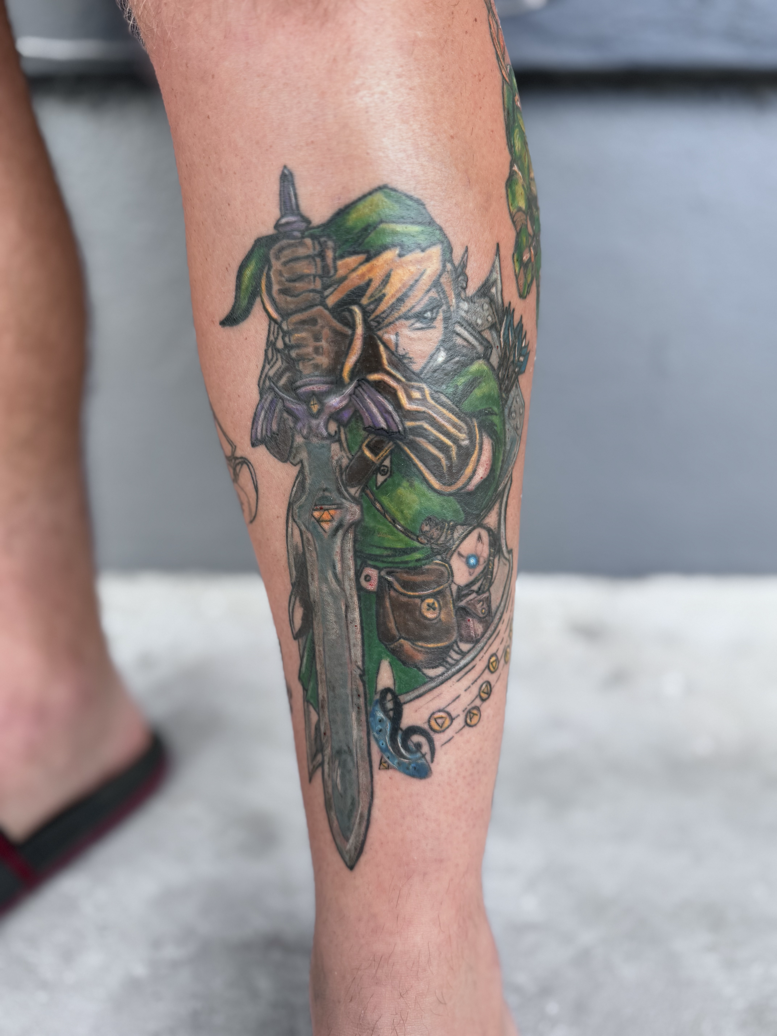 Tattoo of Link from The Legend of Zelda holding a sword, with green clothing and blonde hair, on a person's forearm.