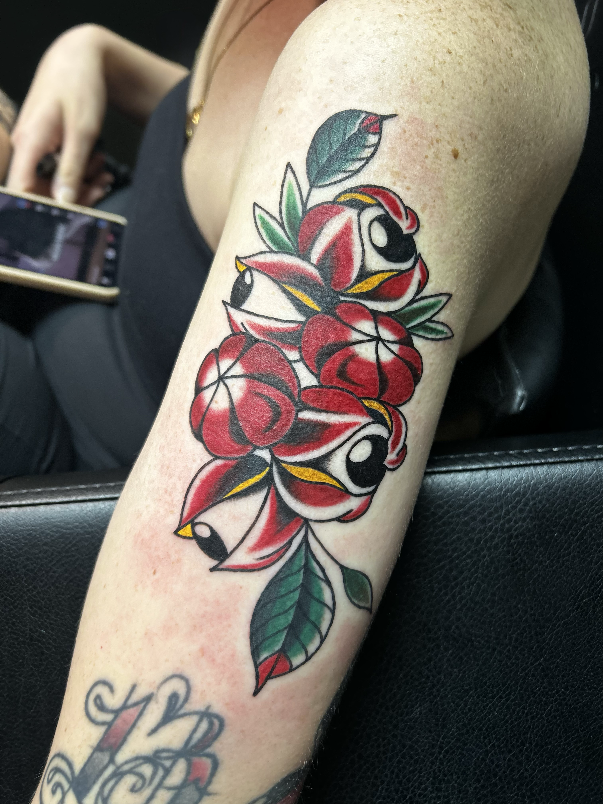 Colorful tattoo of roses and leaves on person's arm, with bold outlines and vibrant red, green, and yellow colors.
