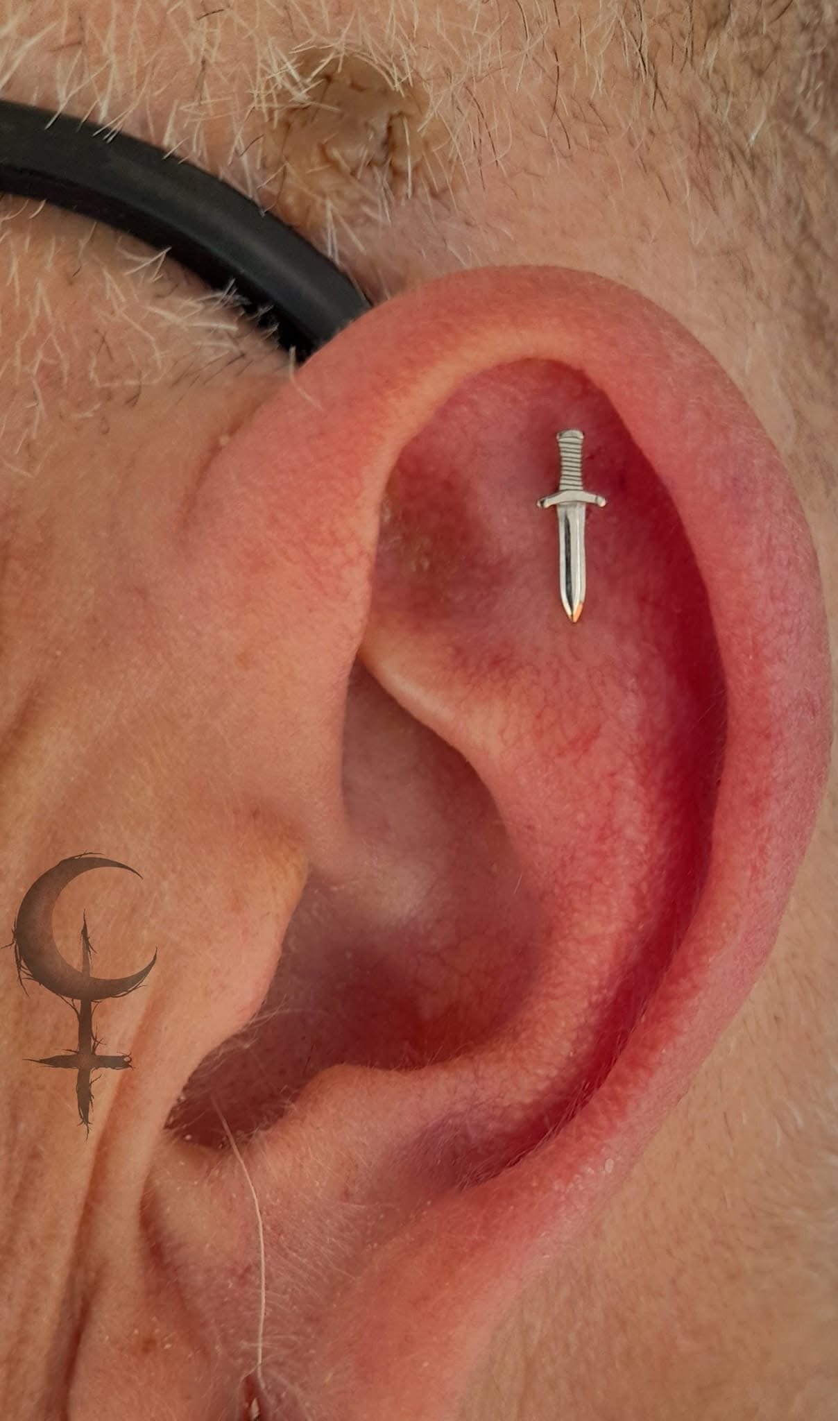 Close-up of a person's ear with a small dagger-shaped jewelry or piercing in the ear piercing hole.