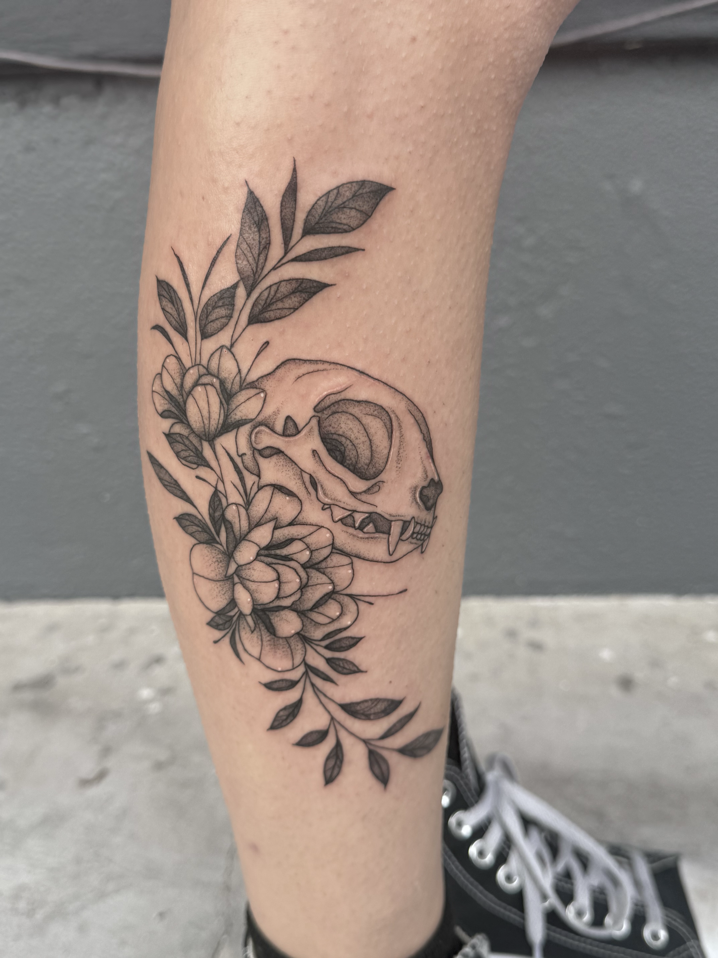 Tattoo of a animal skull surrounded by flowers and leaves on person's leg.