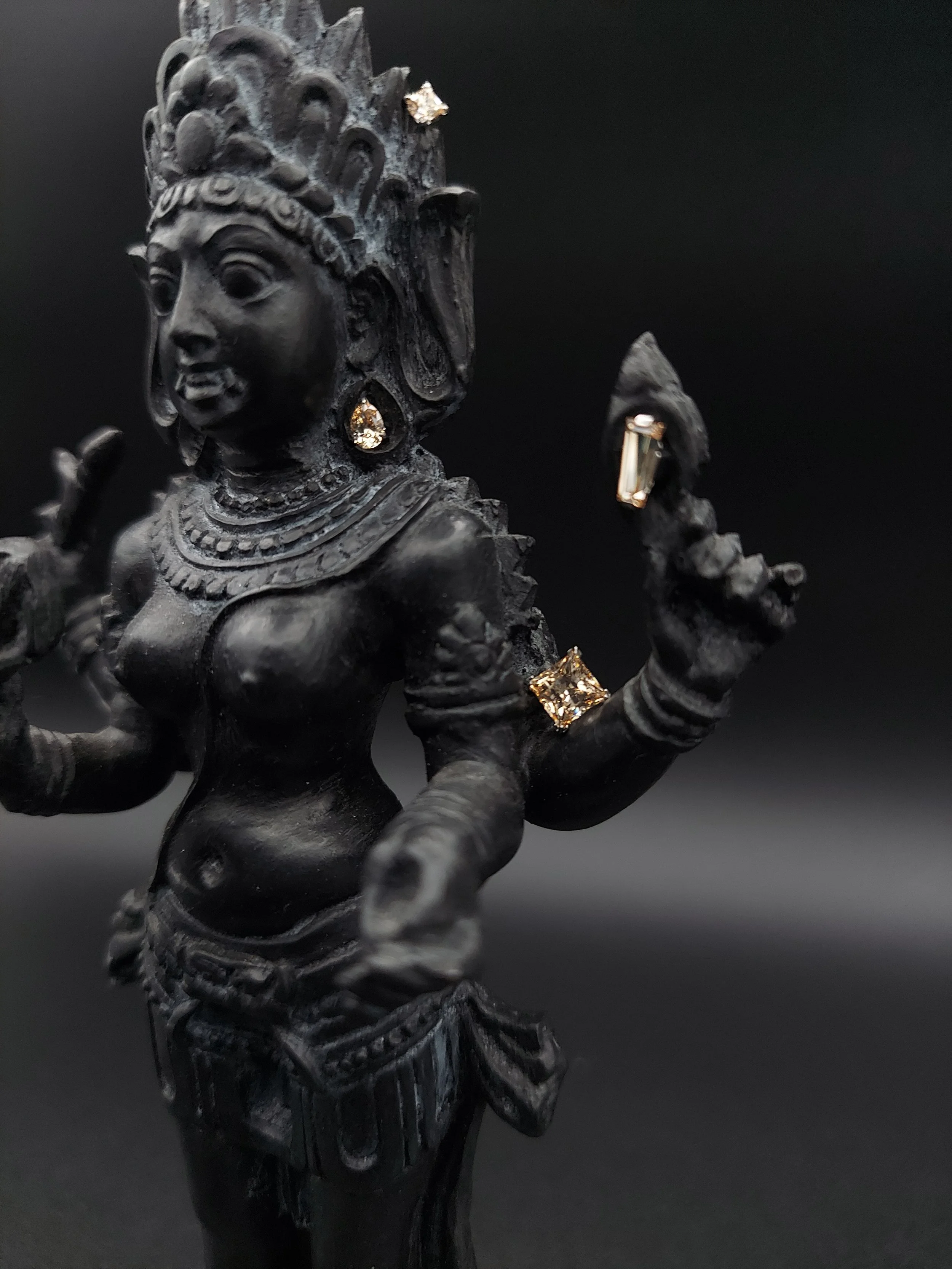 A black statue of a Hindu goddess with intricate carvings and jewelry, set against a dark background.