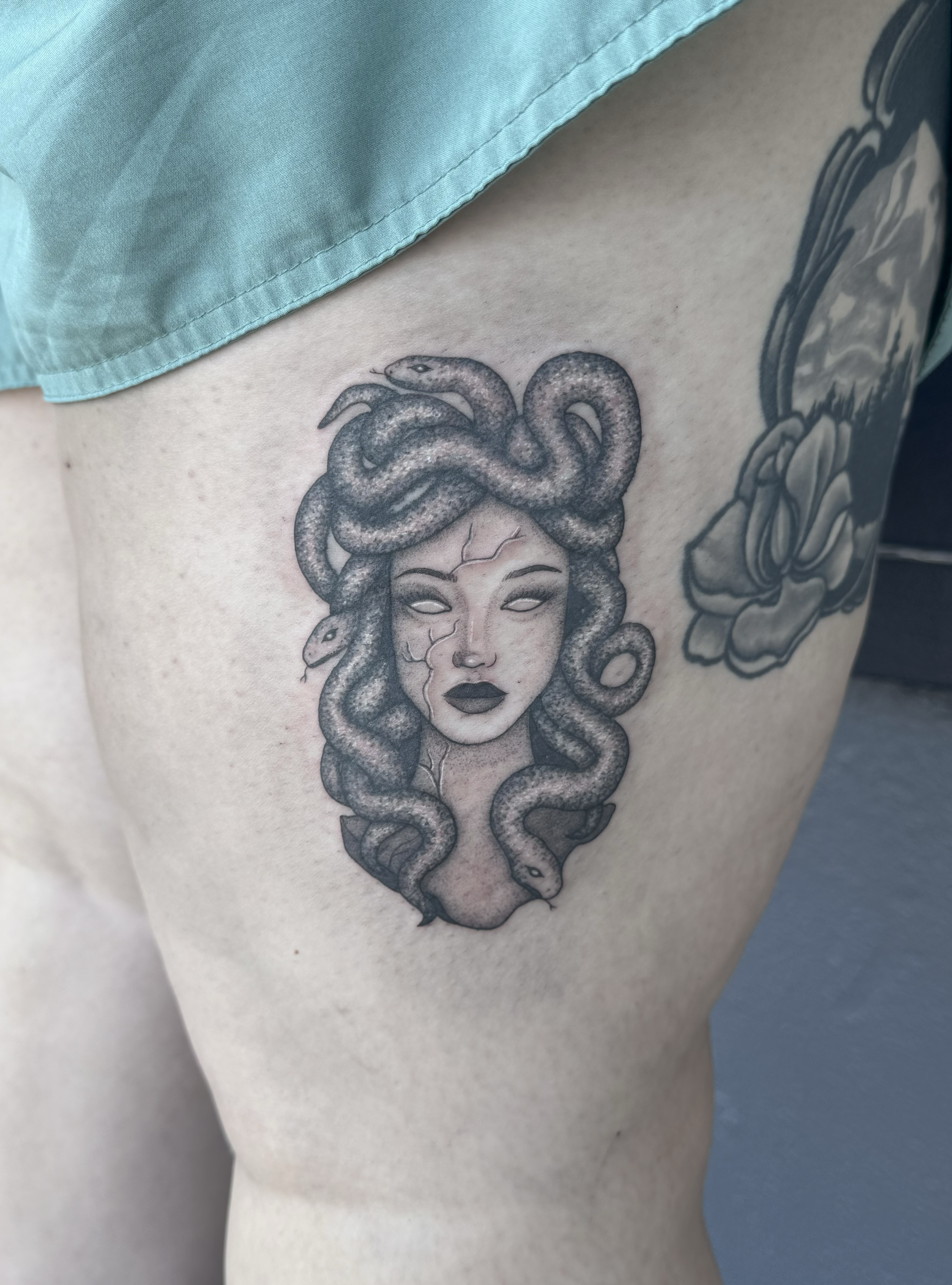 Tattoo of Medusa with snakes for hair and a cracked face, located on a person's upper thigh.