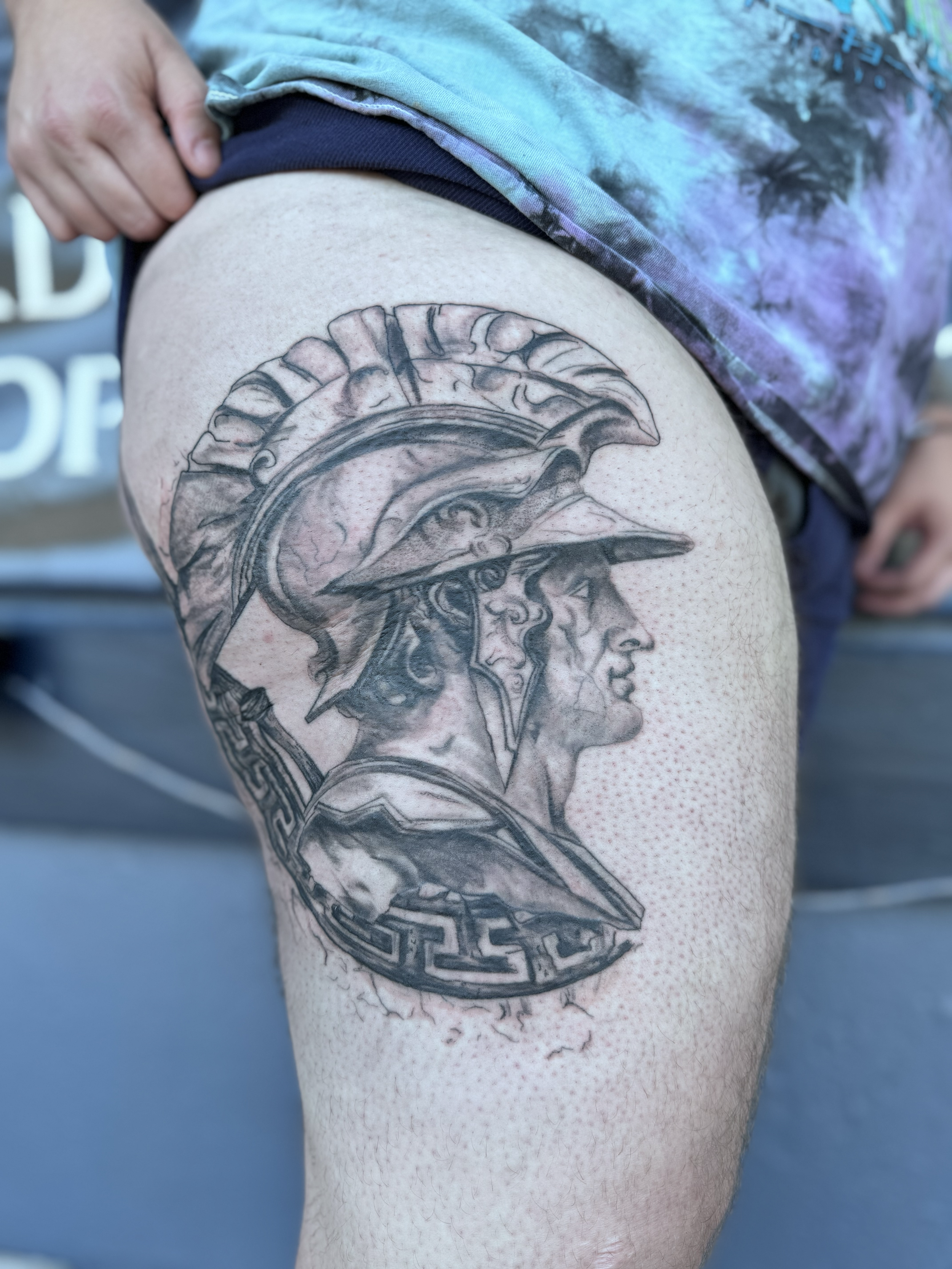 Tattoo of a Roman soldier's profile with detailed helmet, armor, and a Greek key border on the thigh.
