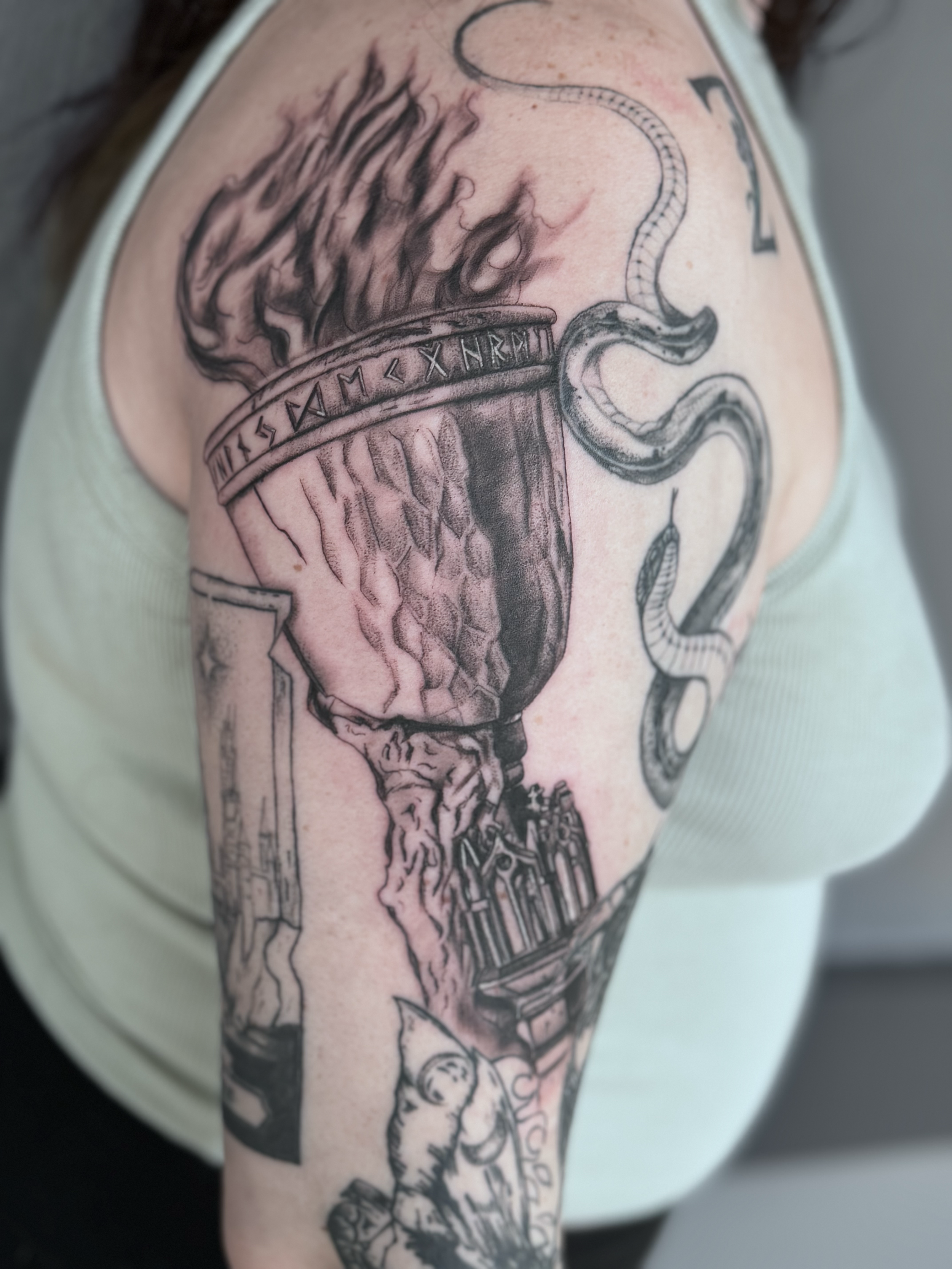 Tattoo of a cup with flames and a snake wrapped around it, featuring Roman numerals and architectural elements.