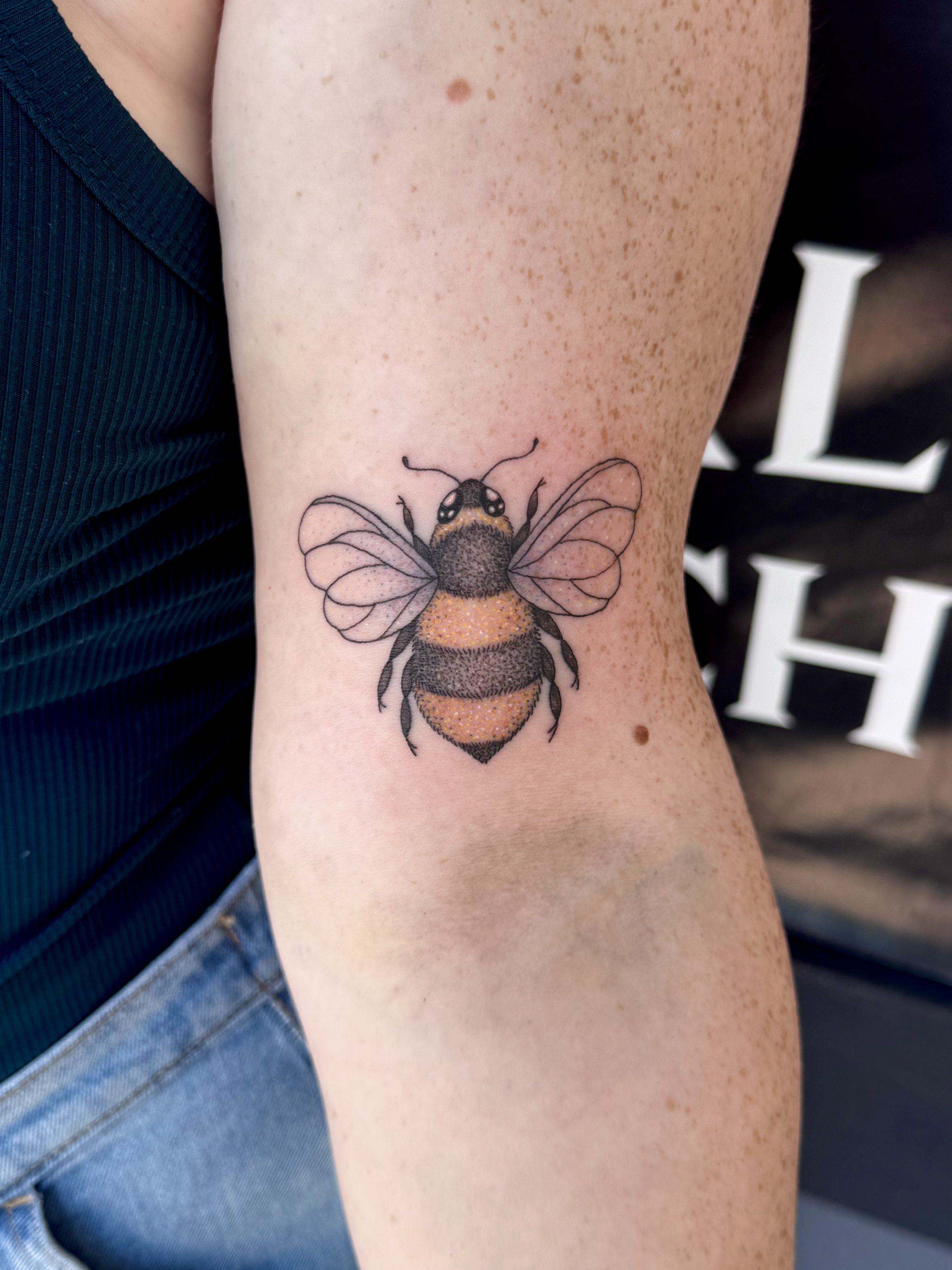 Tattoo of a bee with detailed wings and body, located on a person's upper arm.