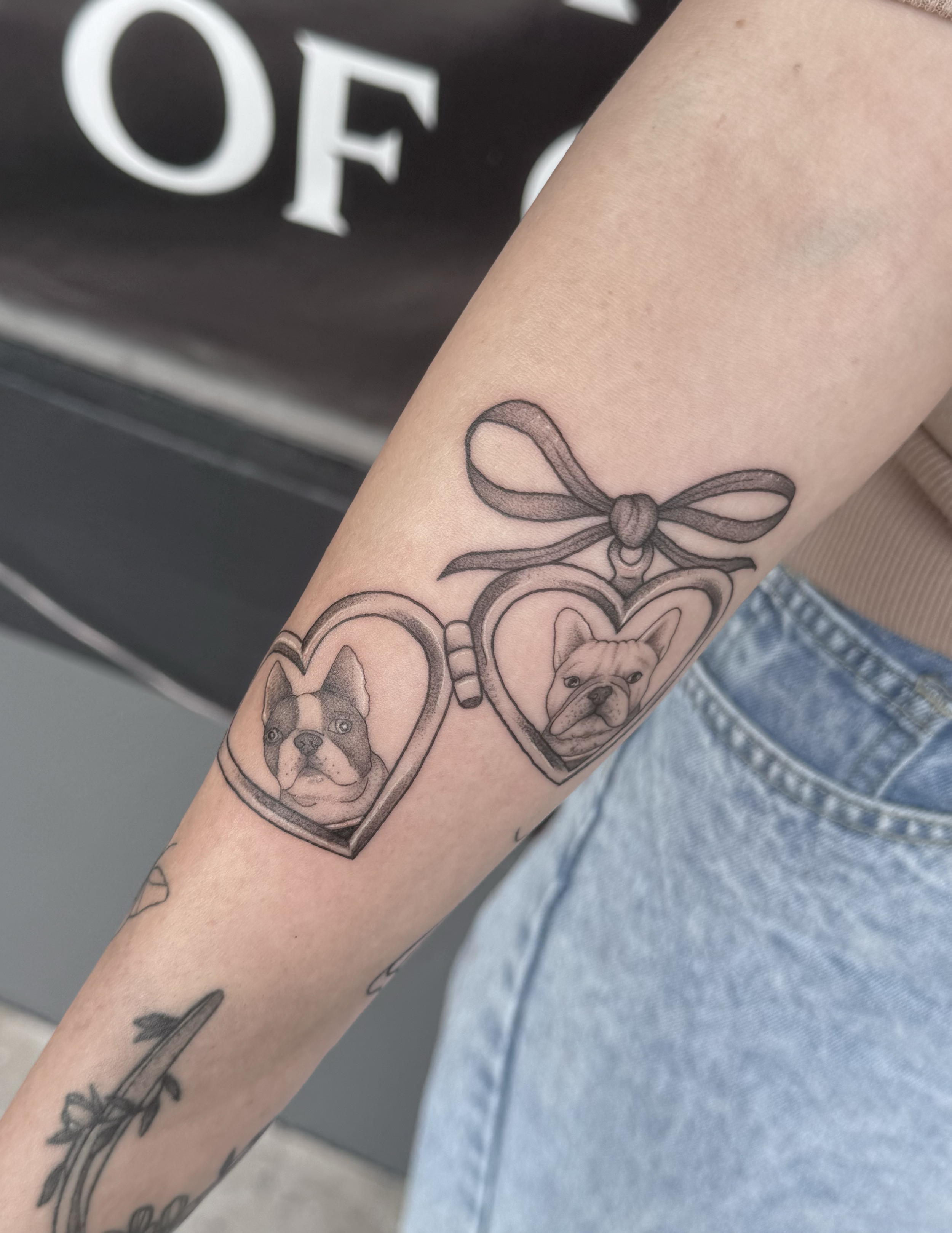 Tattoo of two heart-shaped lockets with dog portraits, connected by a bow on the upper side.