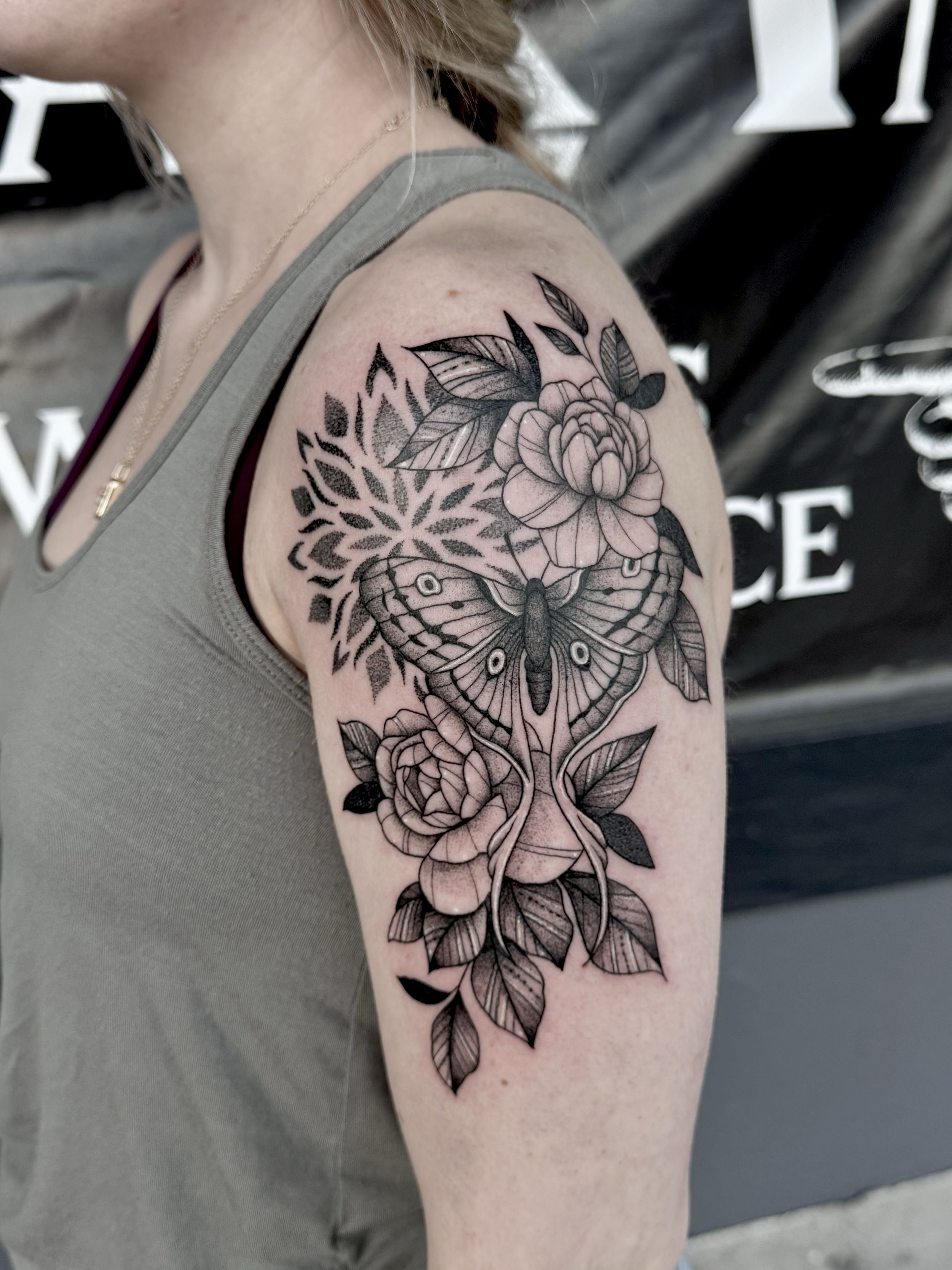 Black and gray floral tattoo on upper arm featuring a butterfly, roses, and leaves.
