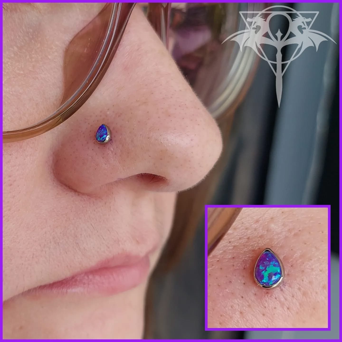 Close-up of a person's face showing a nose piercing with a teardrop-shaped opal gemstone, wearing glasses, with a person in the background.