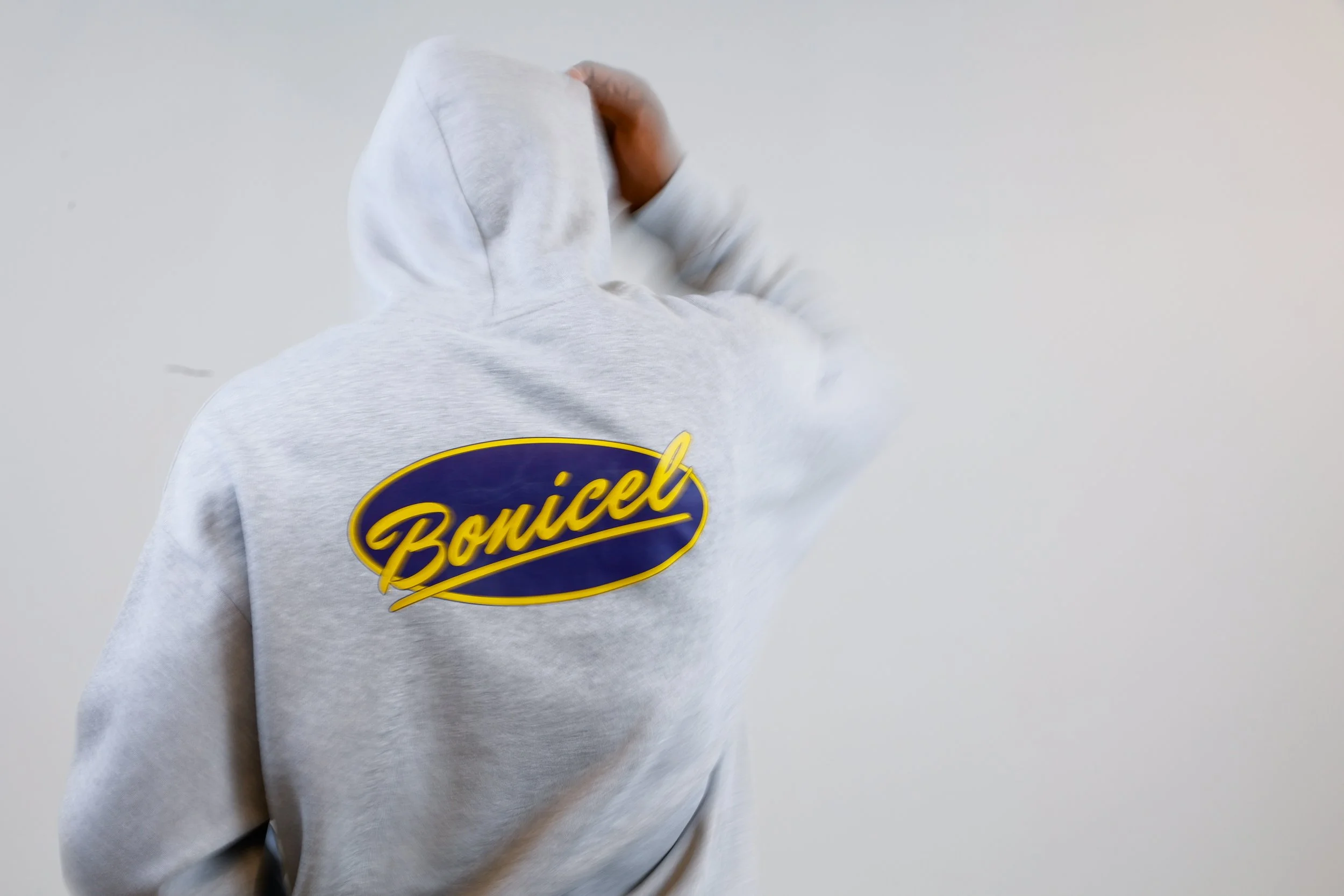 Person wearing a light gray hoodie with a 'BoniceL' logo on the back, standing against a plain white wall, with their hand on their head.