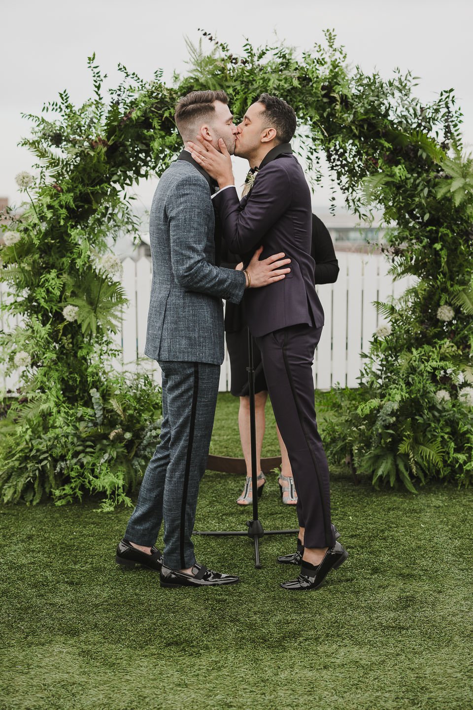 Grooms first kiss in front of lush greenery ceremony arch