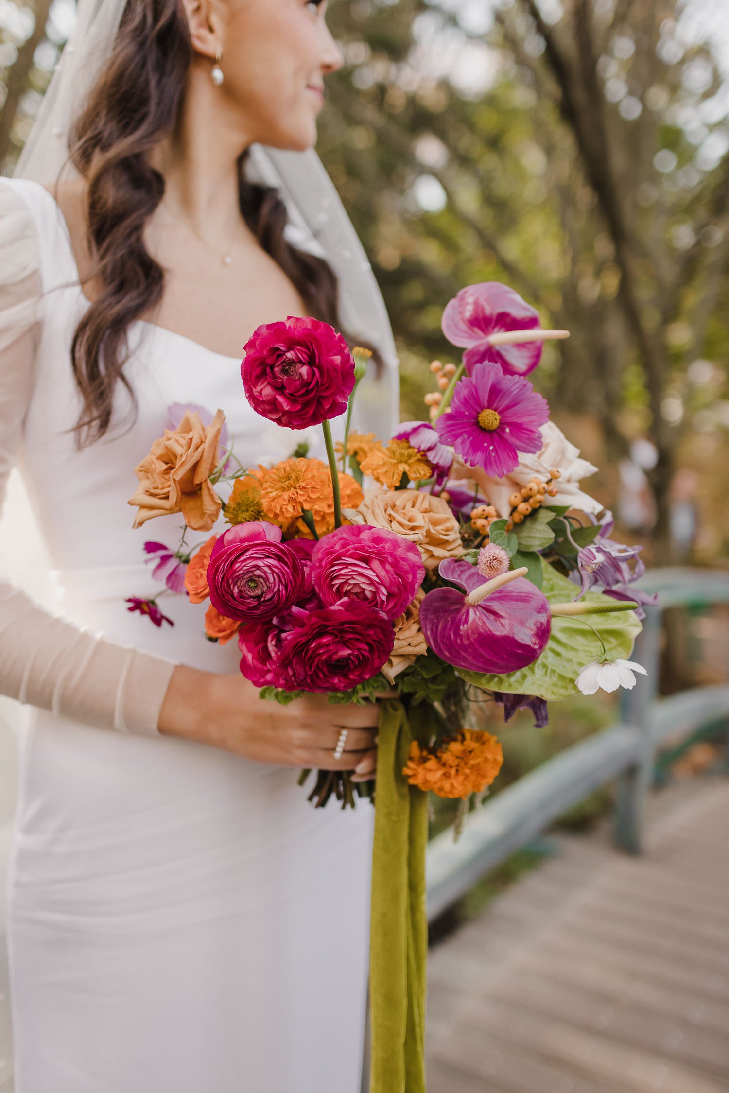 Colorful wedding bouquet with pink ranunculus, orange marigolds, green anthurium lily, and chartreuse velvet ribbon