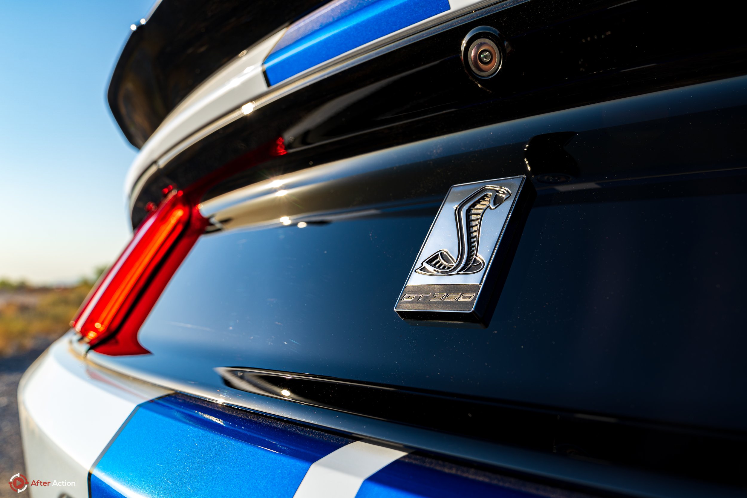 Shelby Cobra emblem on rear tailgate of a white GT350R Mustangs with blue race stripes staged in at Sunrise in desert Photo by After Action, LLC #AfterActionAZ