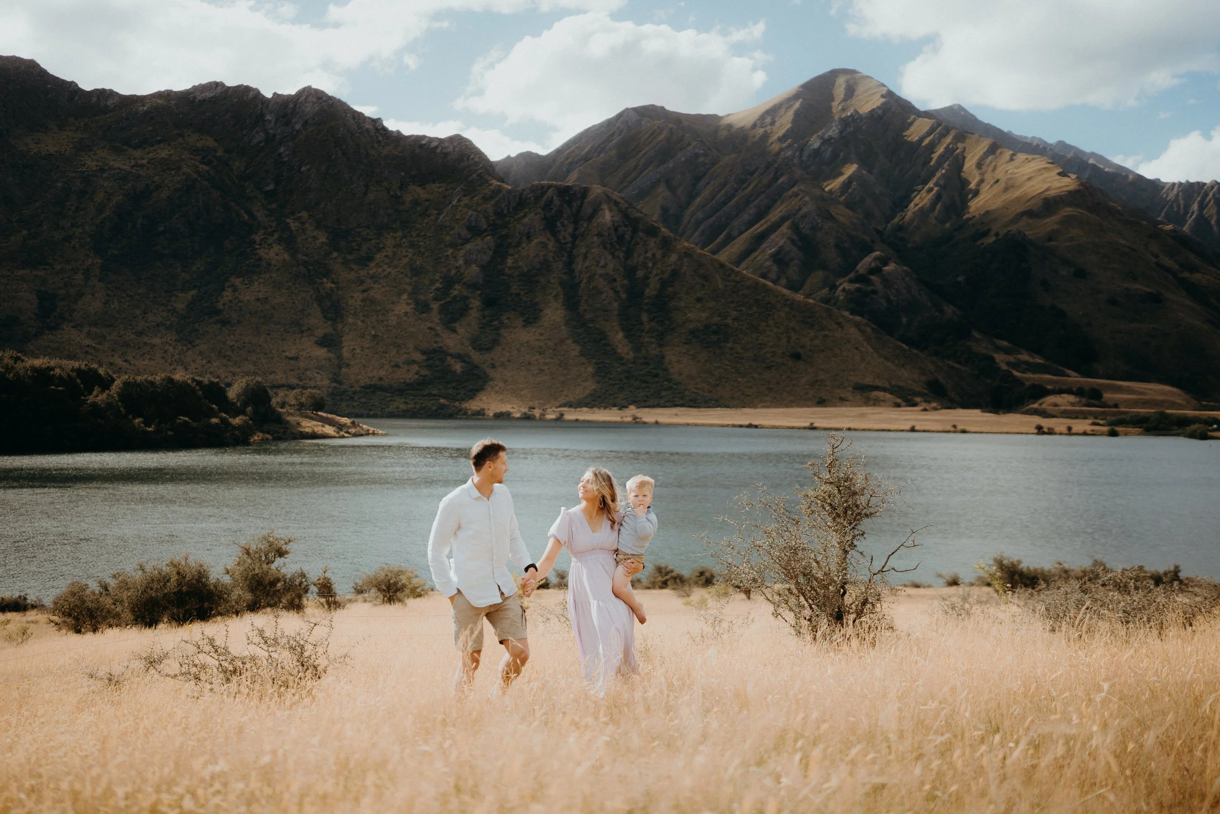 family of 3 walking through golden grass in front of moke lake and ben lomond mountains