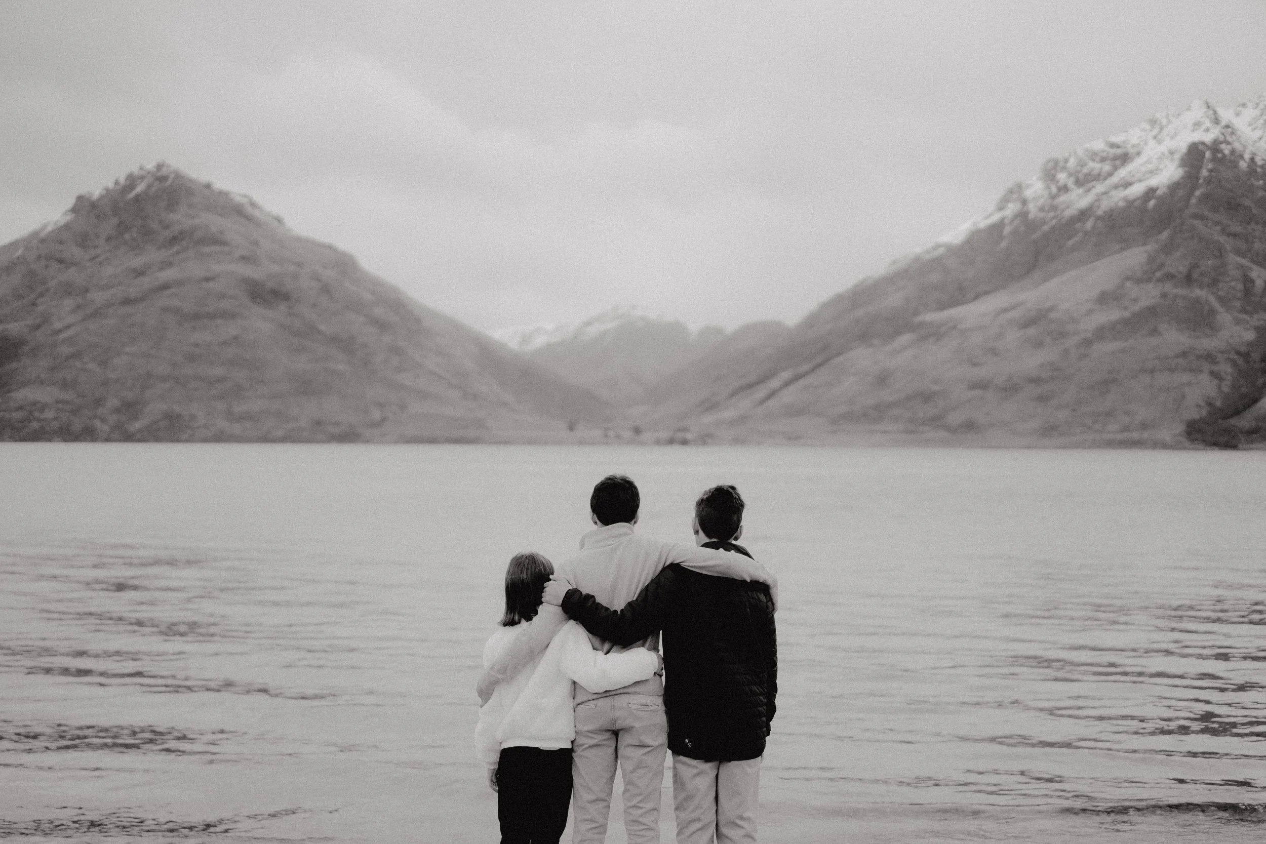 Black and white image of siblings with their arms around eachother admiring Lake Whakatipu