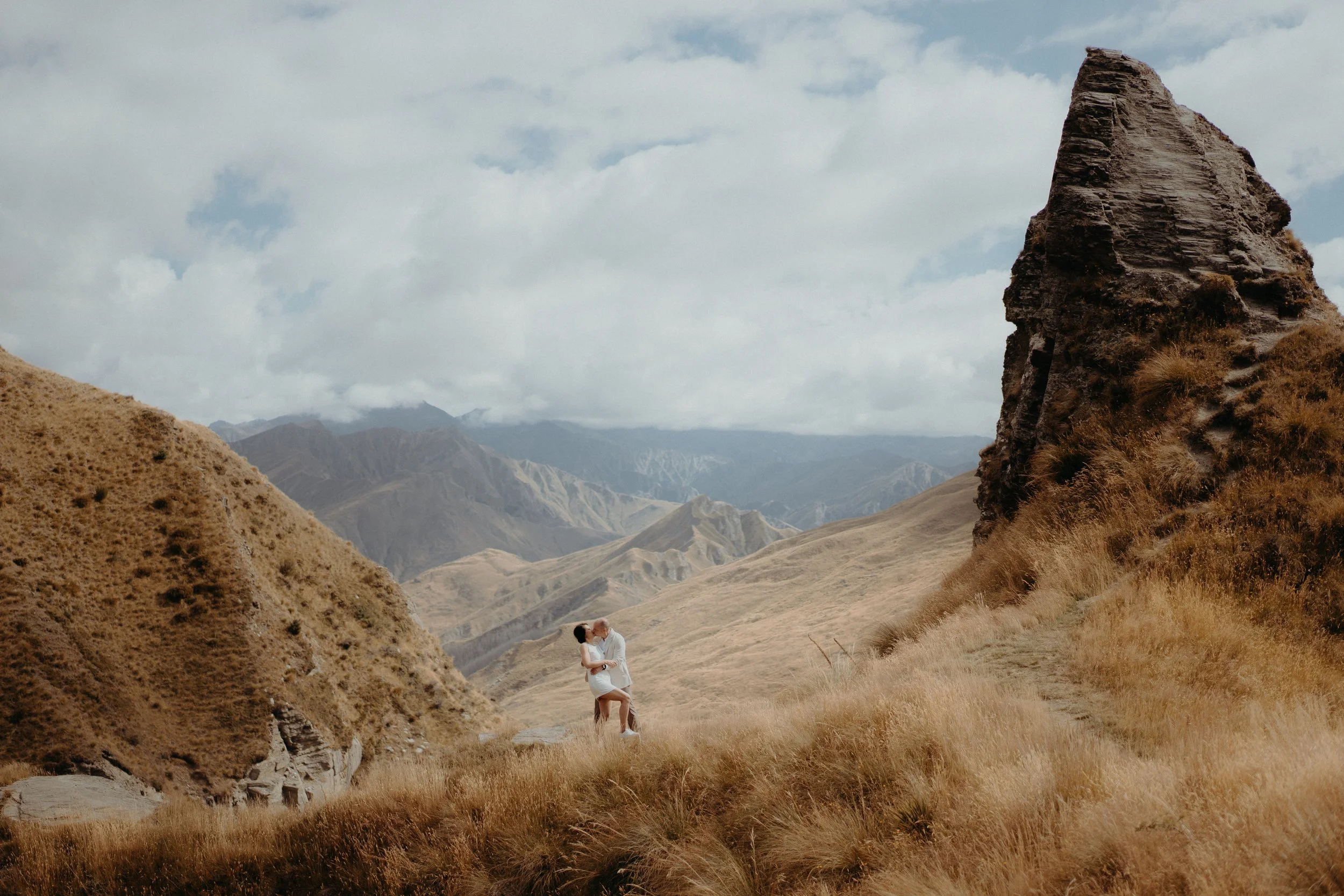 Couple hugging each other on the horizon, standing beside a tall rock