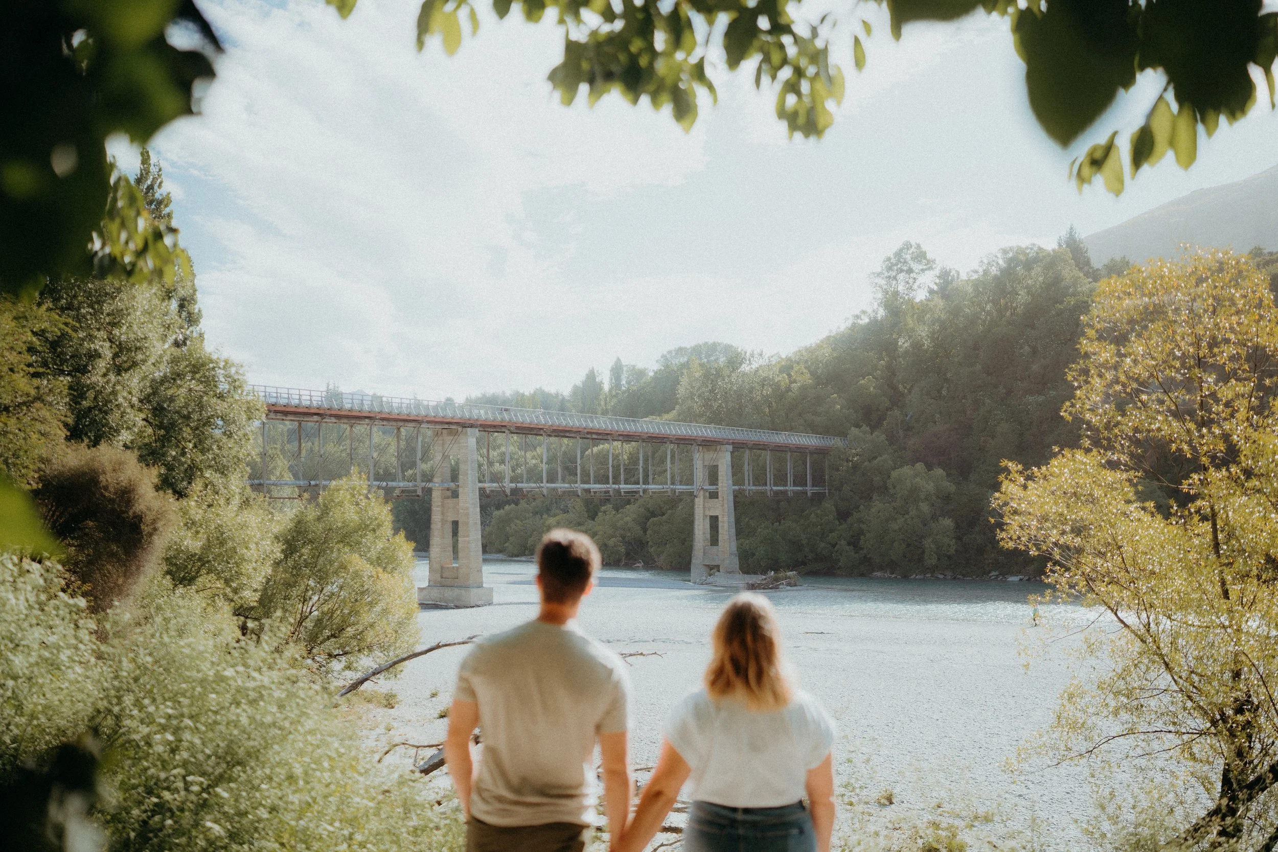 Couple holding hands facing away from camera admiring old shotover bridge
