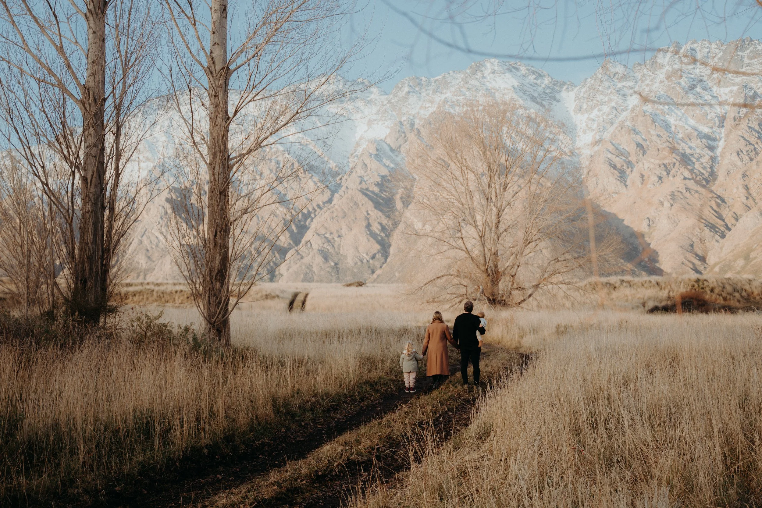 Wide angle of family walking through dried winter grass toward snow filled remarkable mountains