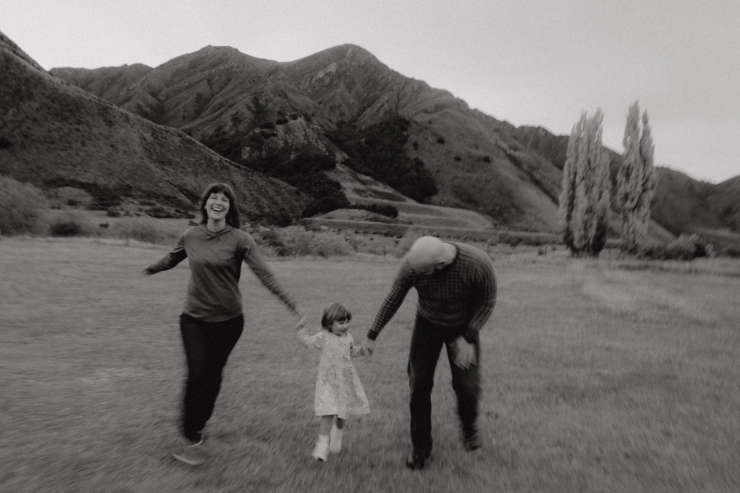Black and white image of family of 3 running through grassy field