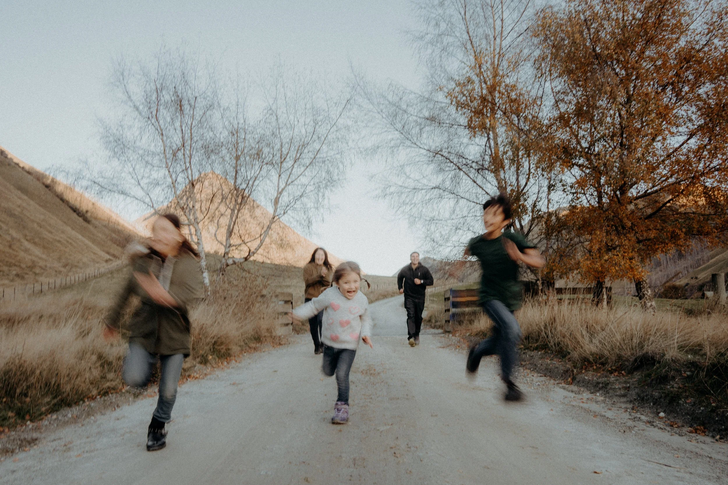 Children running on a dirt path along moke lake road with autumn trees and hills in the background.