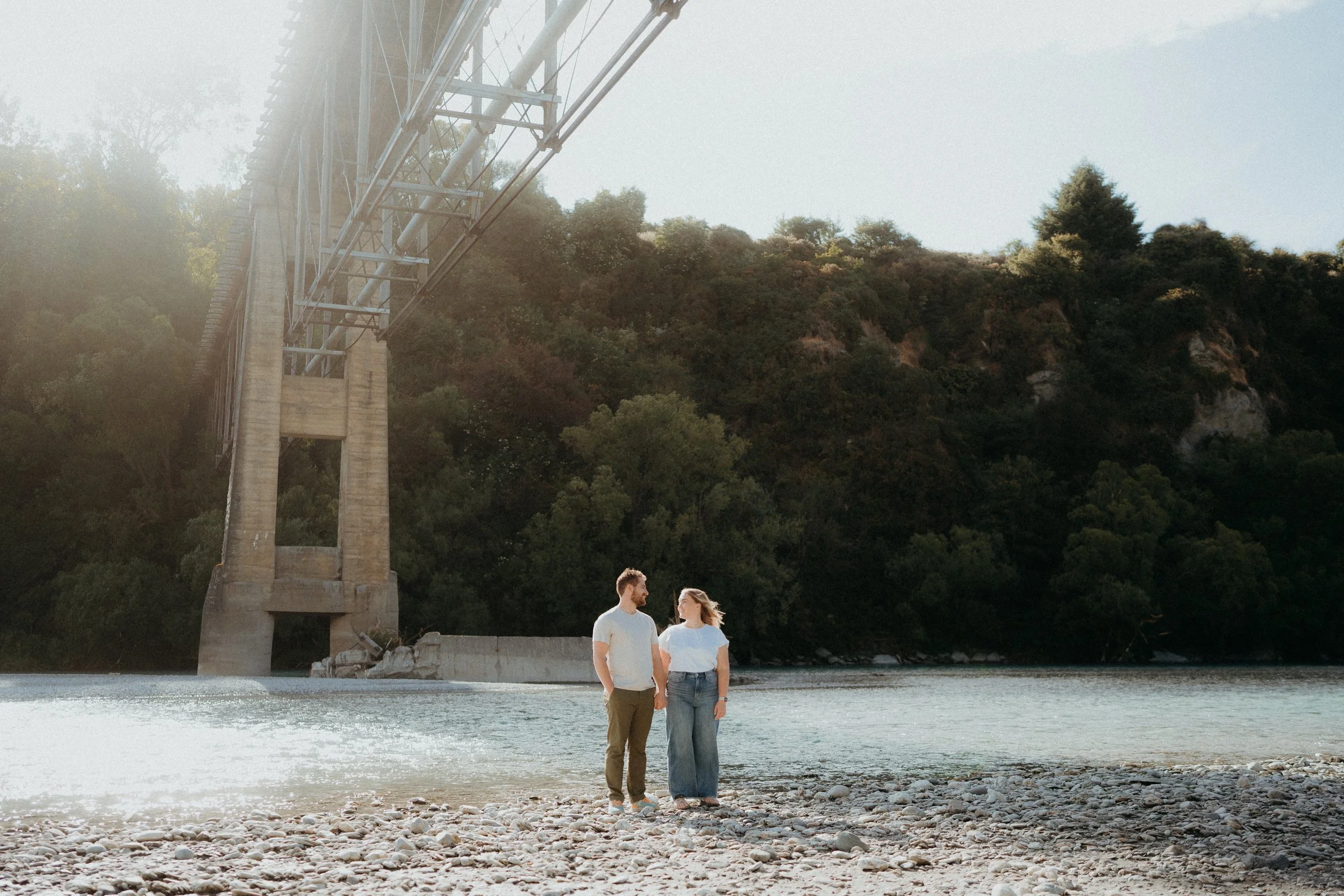 Wide angle photo of couple looking at eachother and posing in front of old shotover bridge
