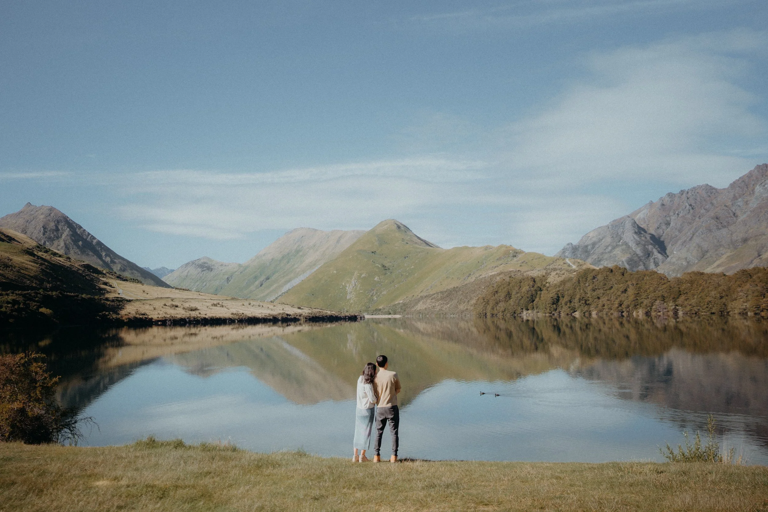 Couple leaning on eachother admiring moke lake on a summers day