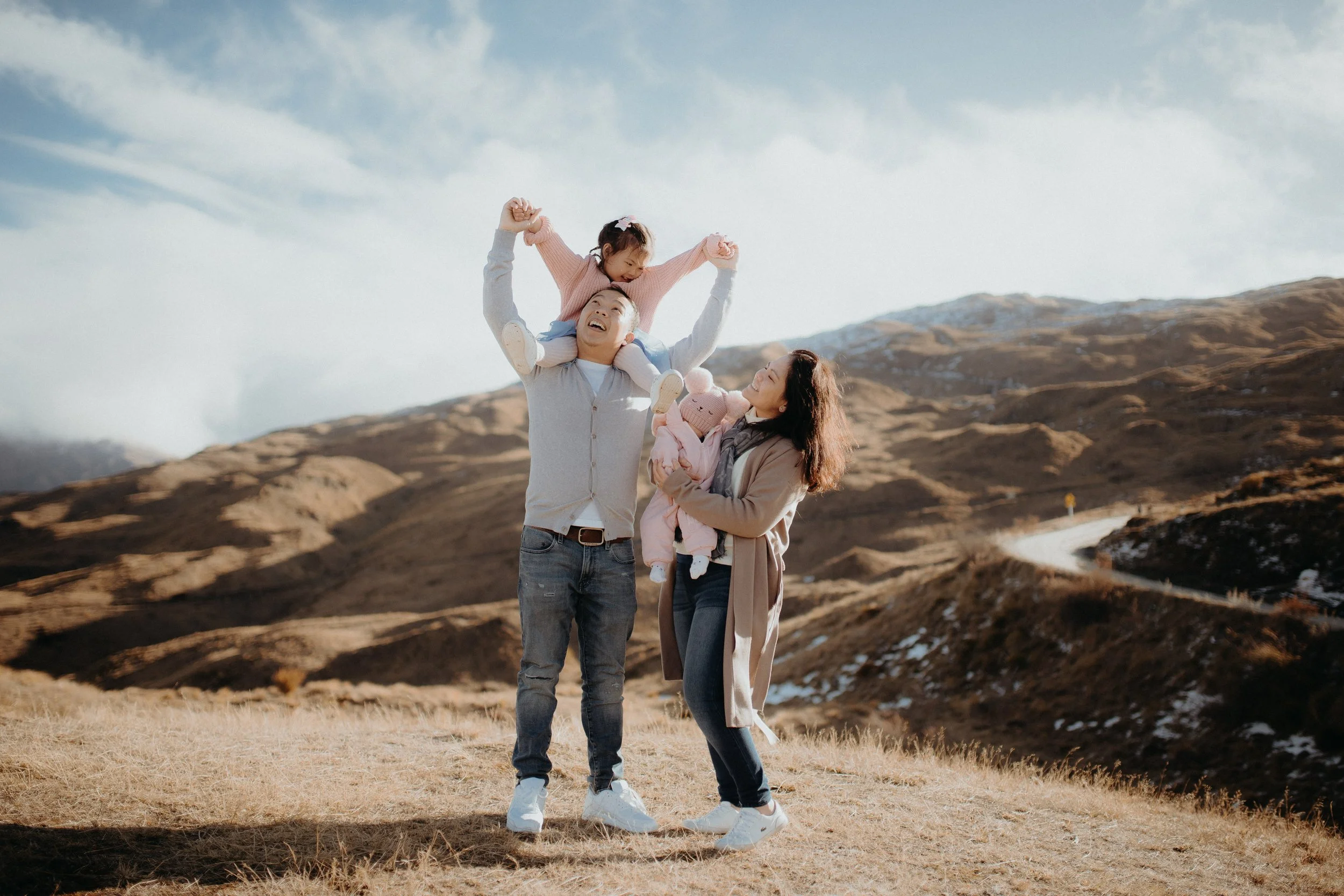 Family posing in front of mountains with child on Dads shoulders
