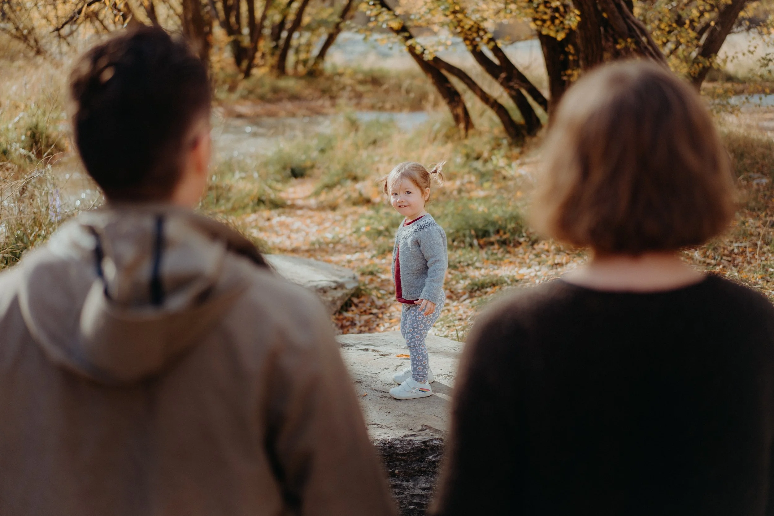 Mother and father facing away from camera, watching daughter play.