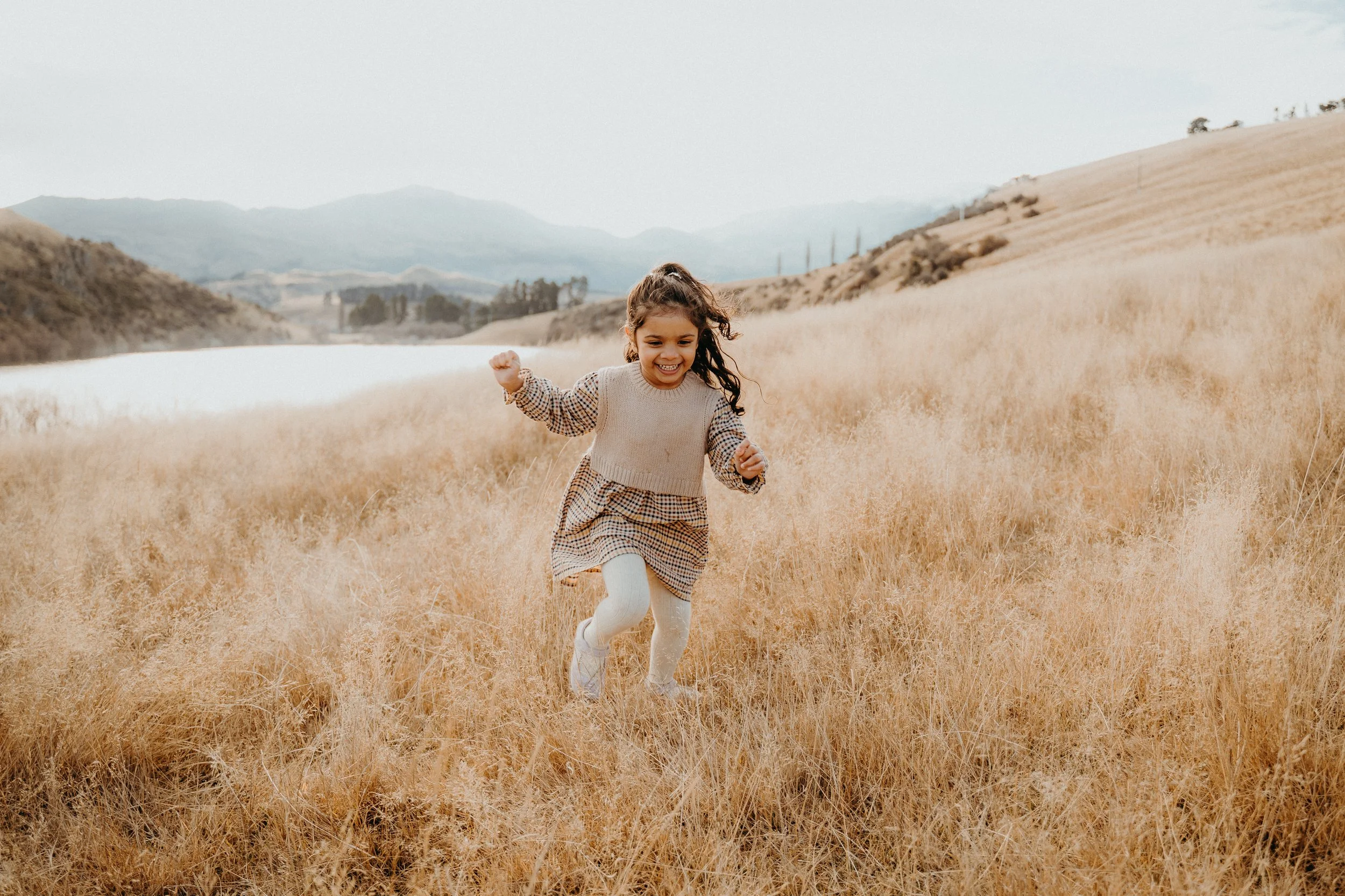 Young girl running through a field of tall, dry grass alongside lake johnson