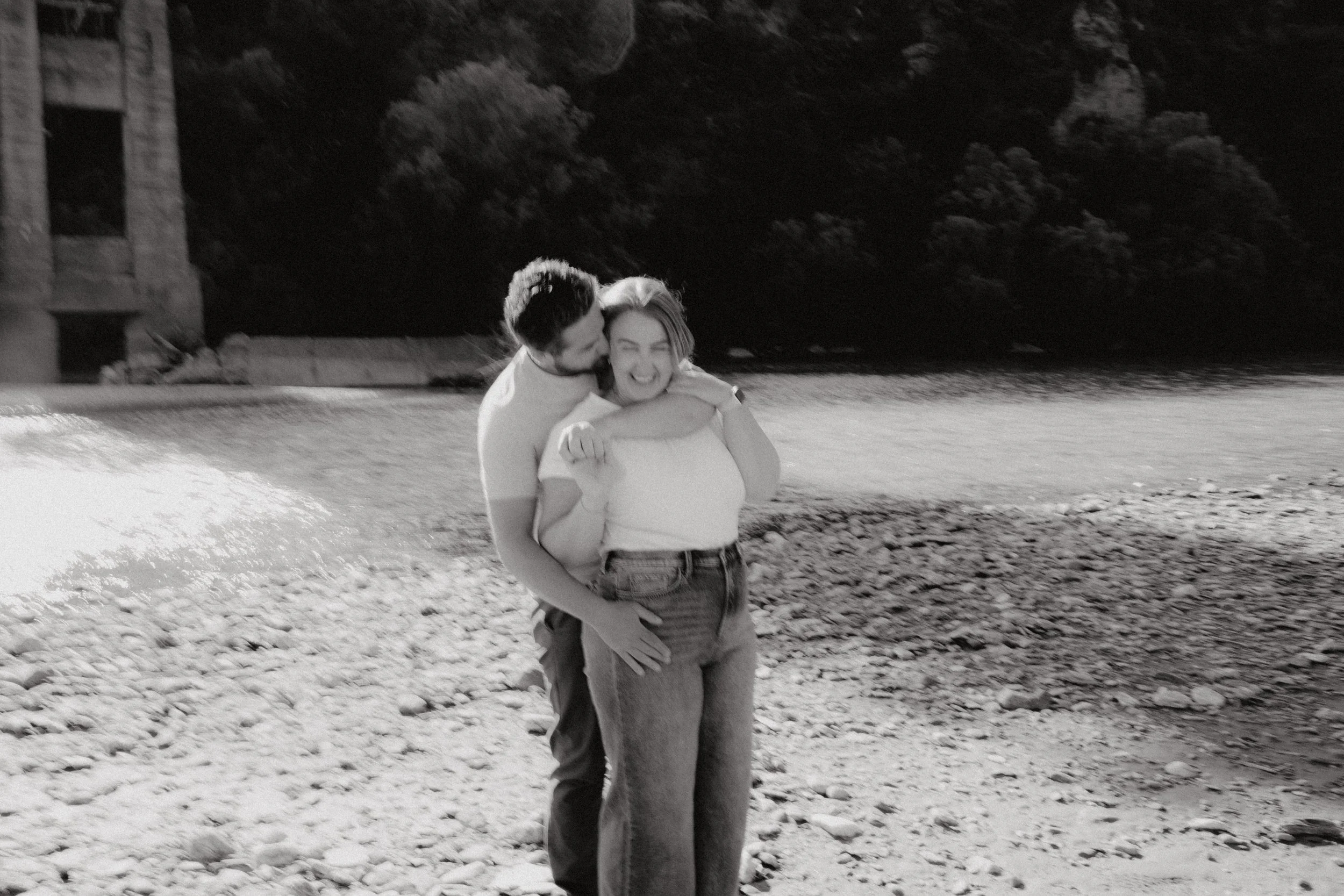 Black and white image of a young couple hugging and laughing together.