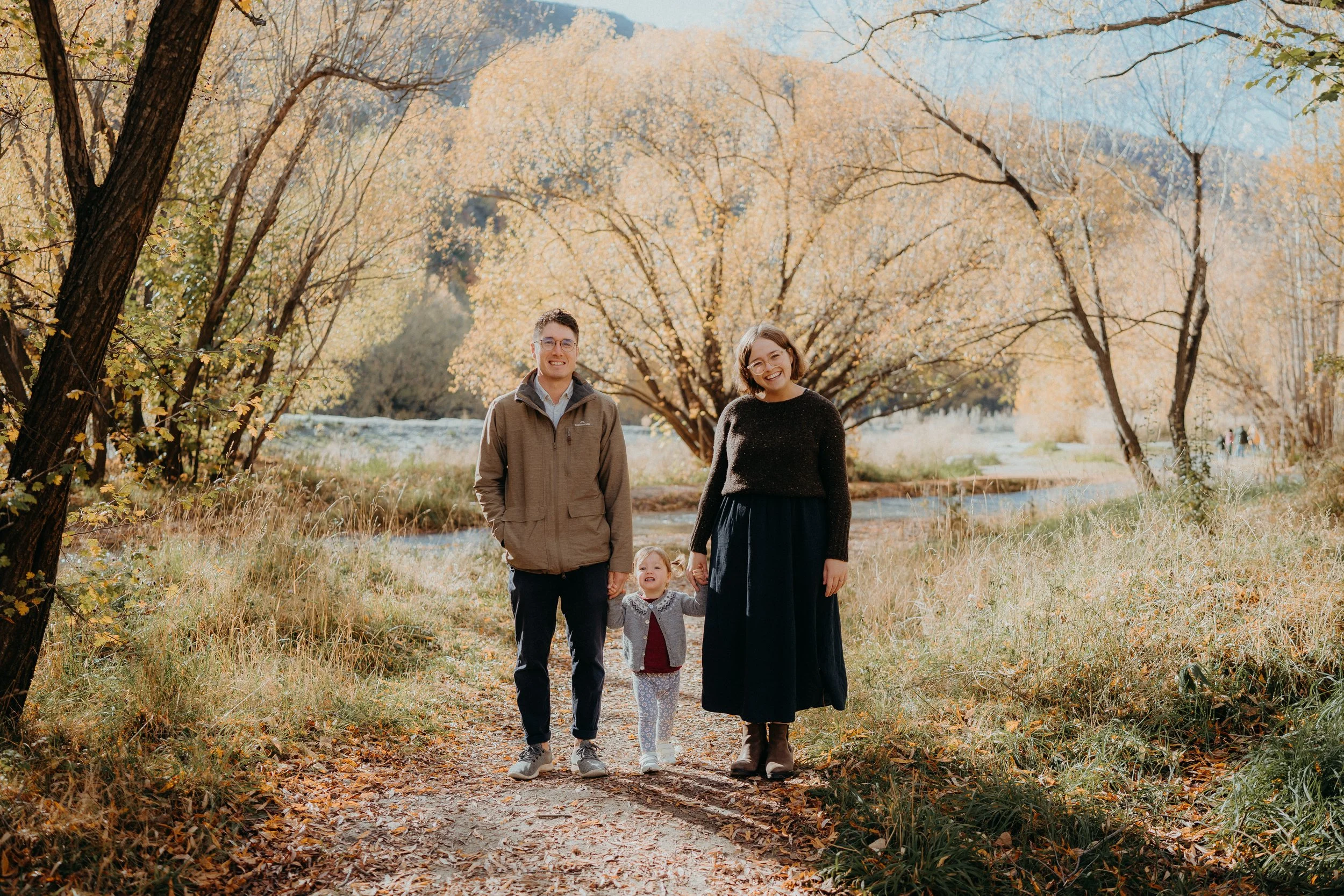 Two parents holding their daughters hand posing by Arrowtown river
