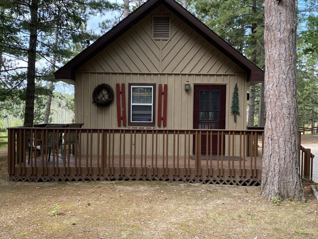 A small wood cabin with a front porch surrounded by trees.