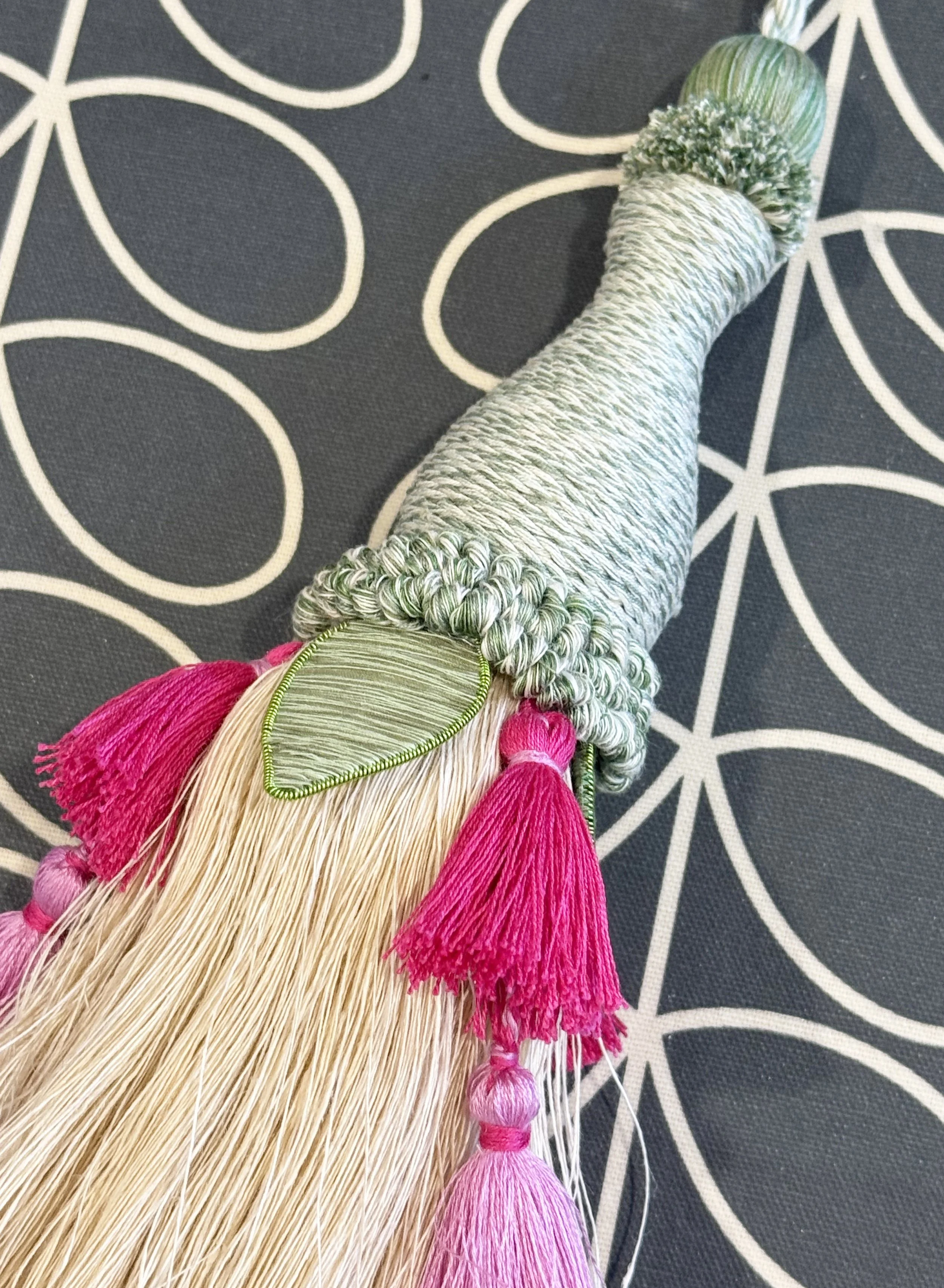 Close-up view of a handmade green, pink and beige tassel made by a student during Elizabeth Ashdown's tassel making workshop