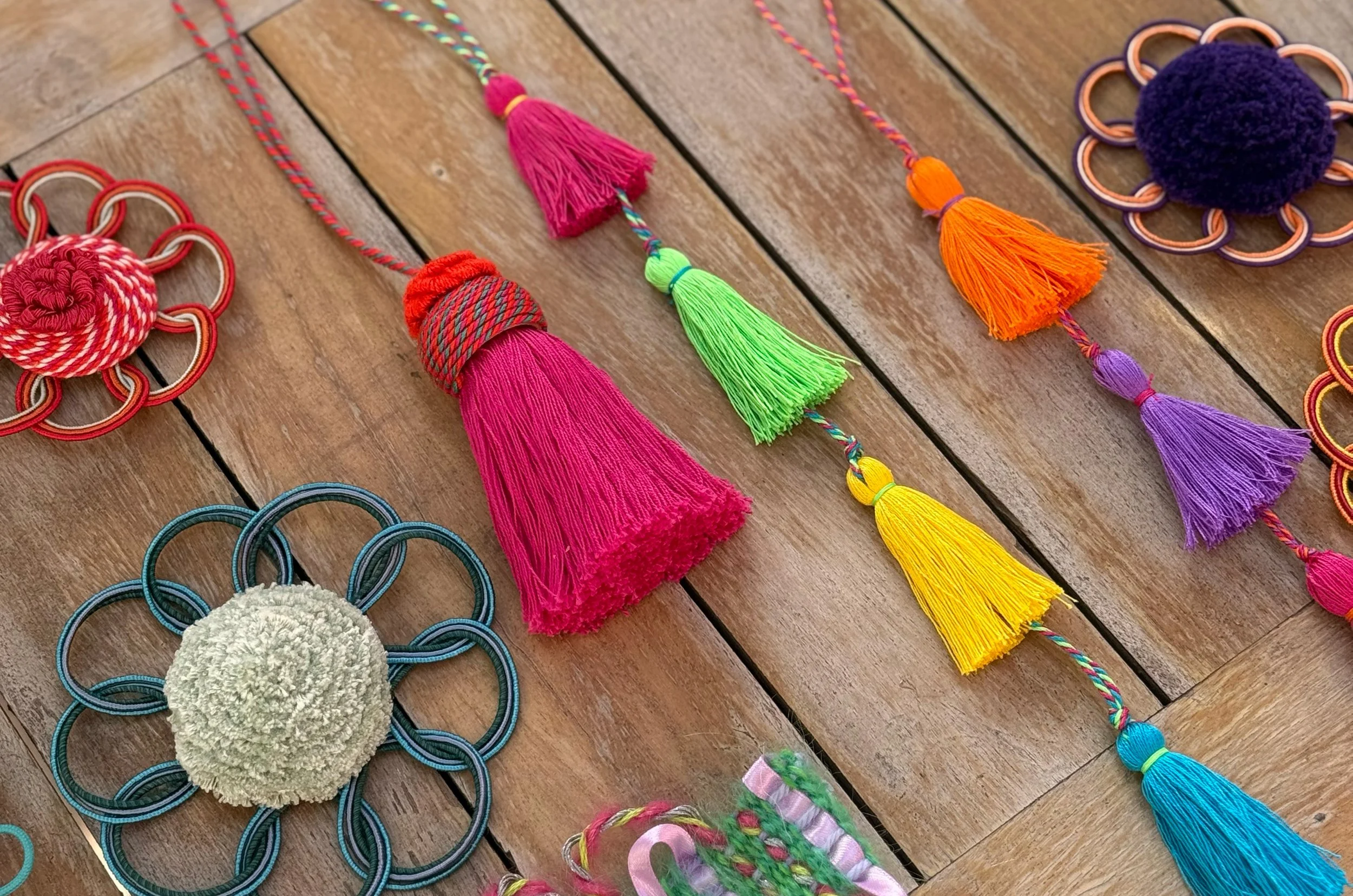 A collection of student passementerie from the Royal School of Needlework masterclass, including bright tassels in pink, green, yellow, orange, purple and turquoise, looped rosettes and hand-woven braids.
