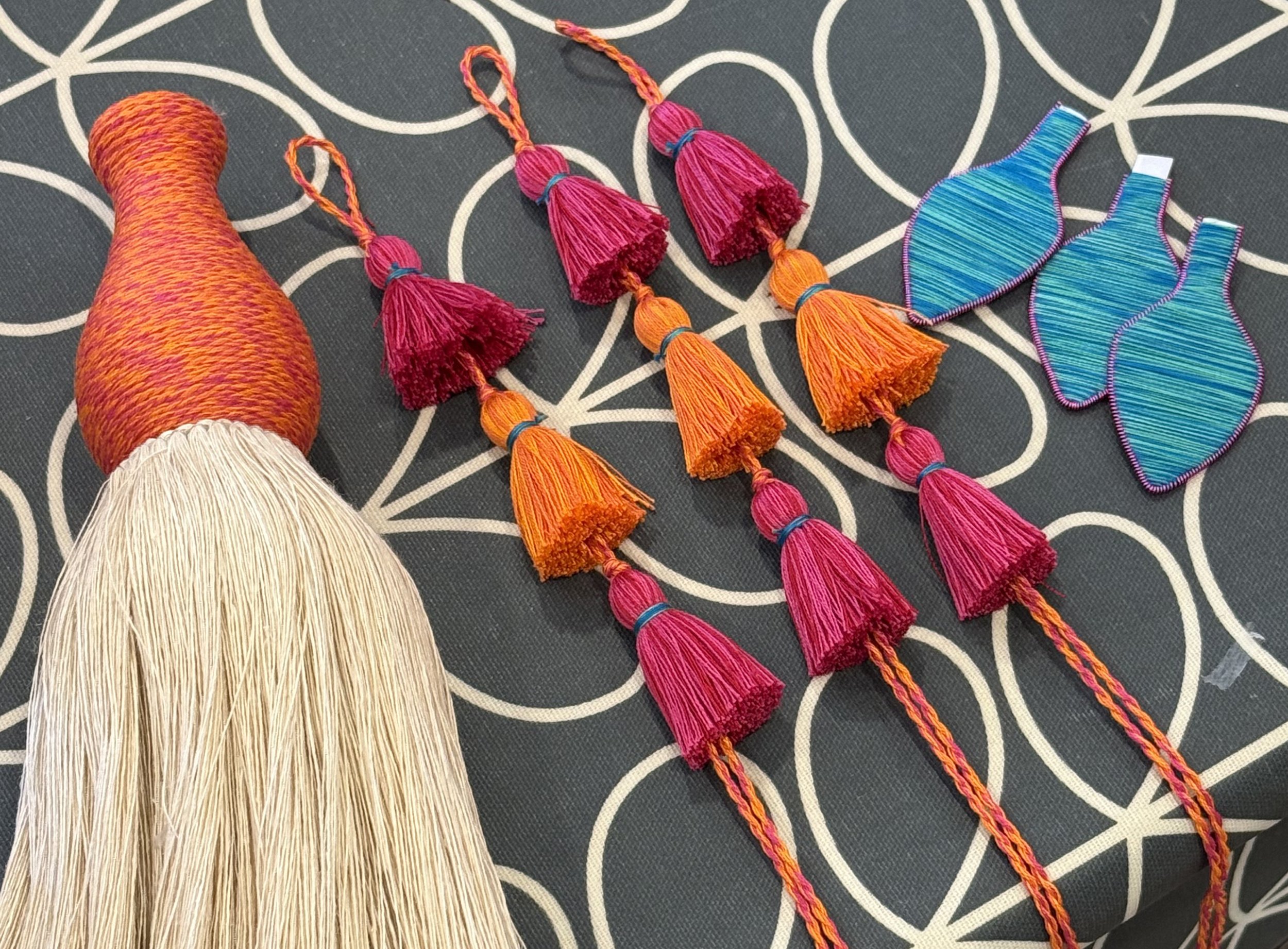 Handmade tassel being created using cartisan leaves in bright blue and pink, strings of mini tassel in shades of hot pink and orange and a linen tassel skirt being assembled.