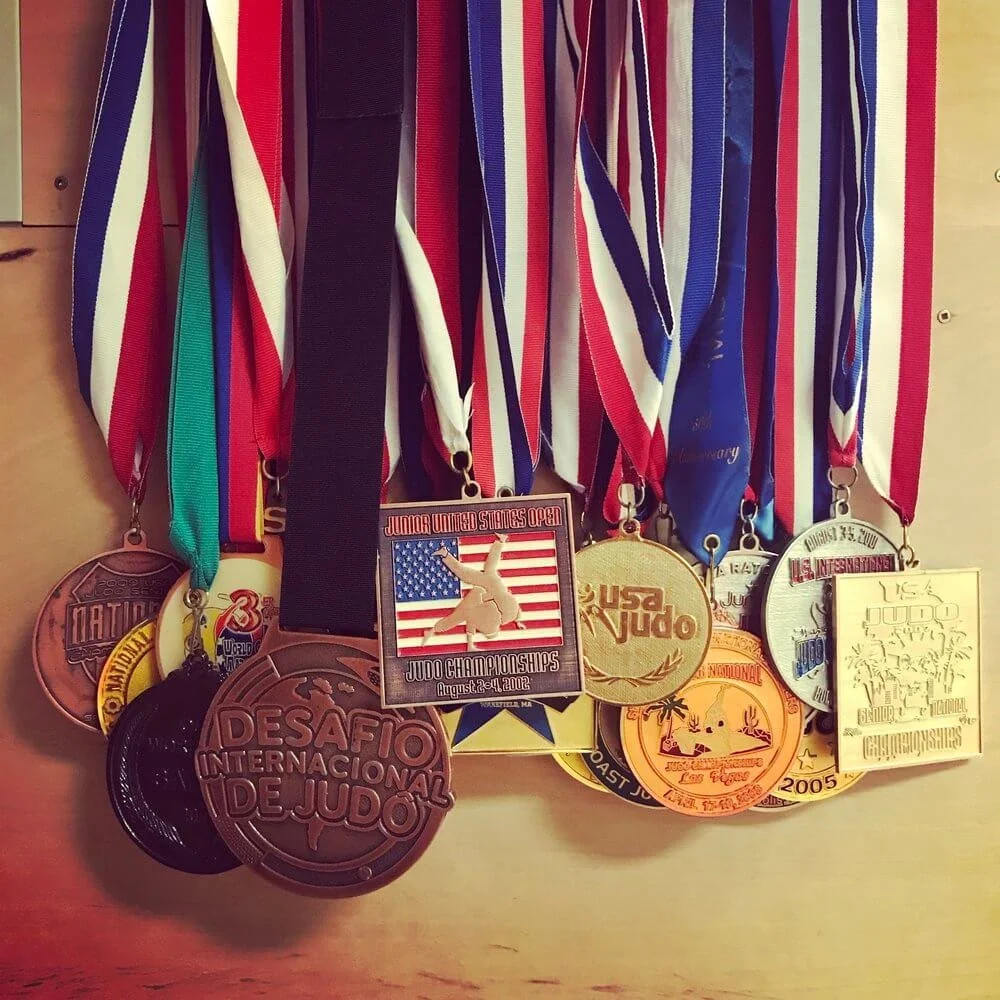 A collection of judo medals hanging on a wooden surface, with various ribbon colors and designs.