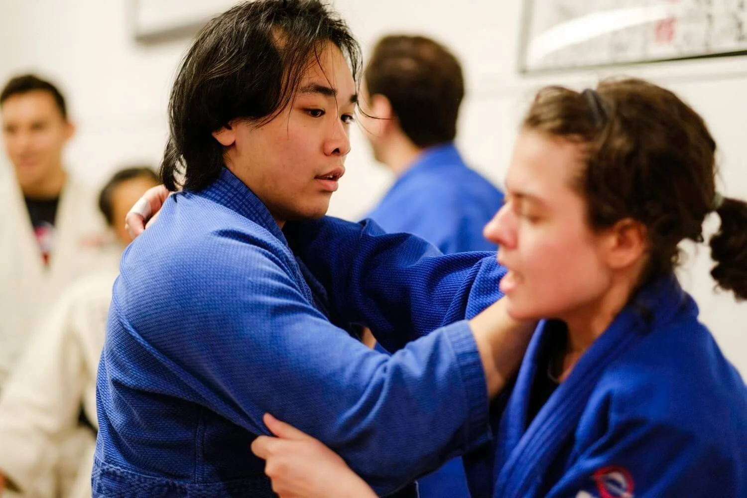 Two martial artists in blue gis practicing a technique in a dojo, with one person grabbing the other's collar.
