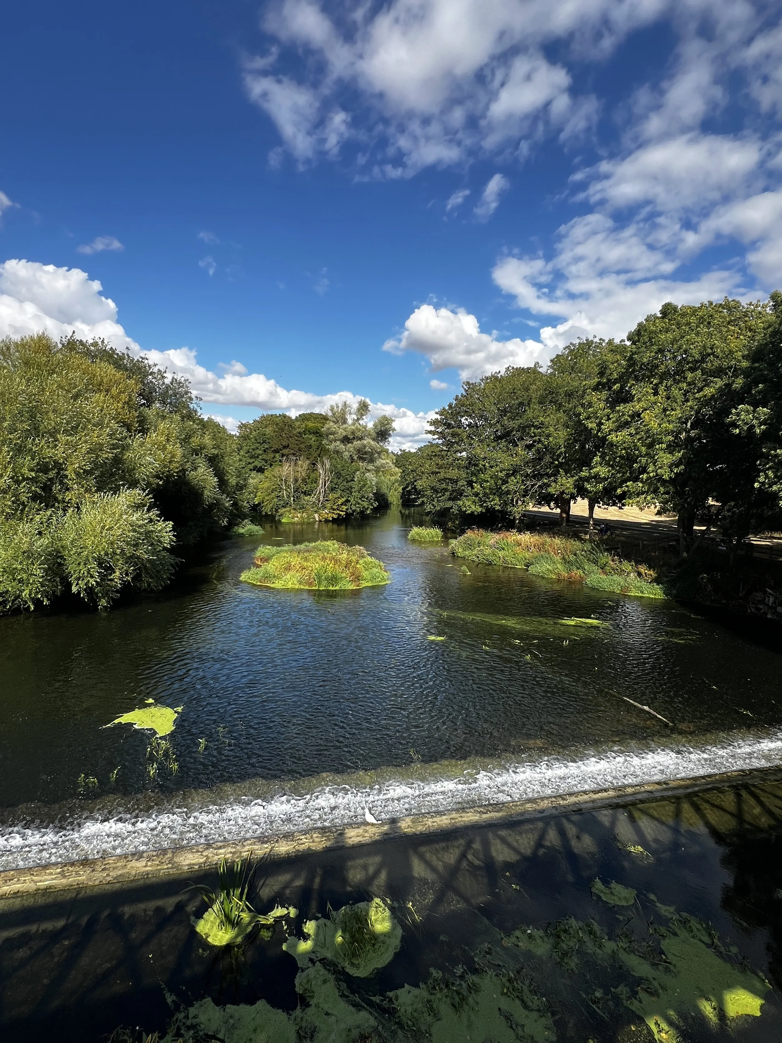 wide river view on sunny day, revealing three people in shadow looking from the bridge
