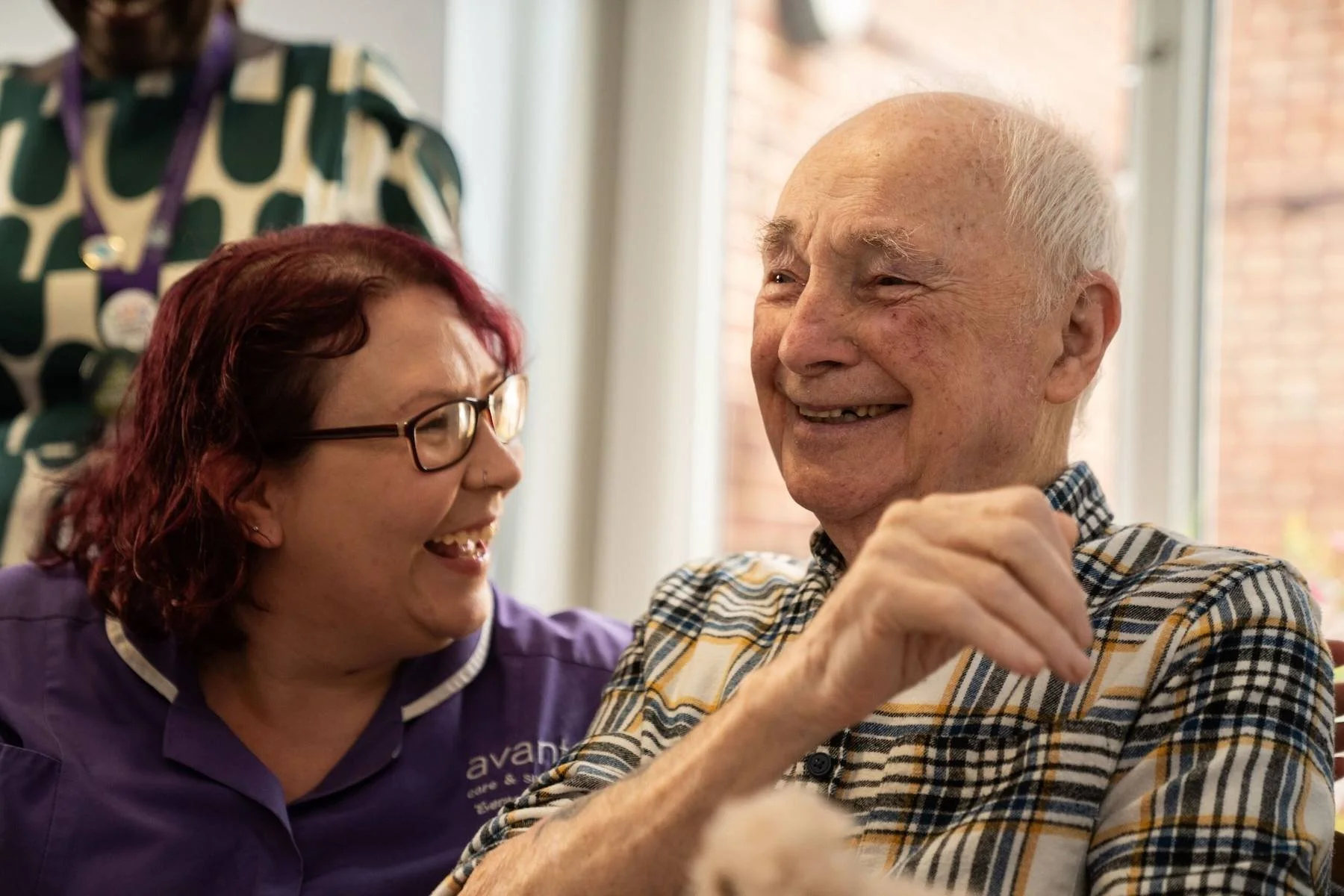 An elderly man and a woman with red hair and glasses are smiling and sharing a joyful moment together.