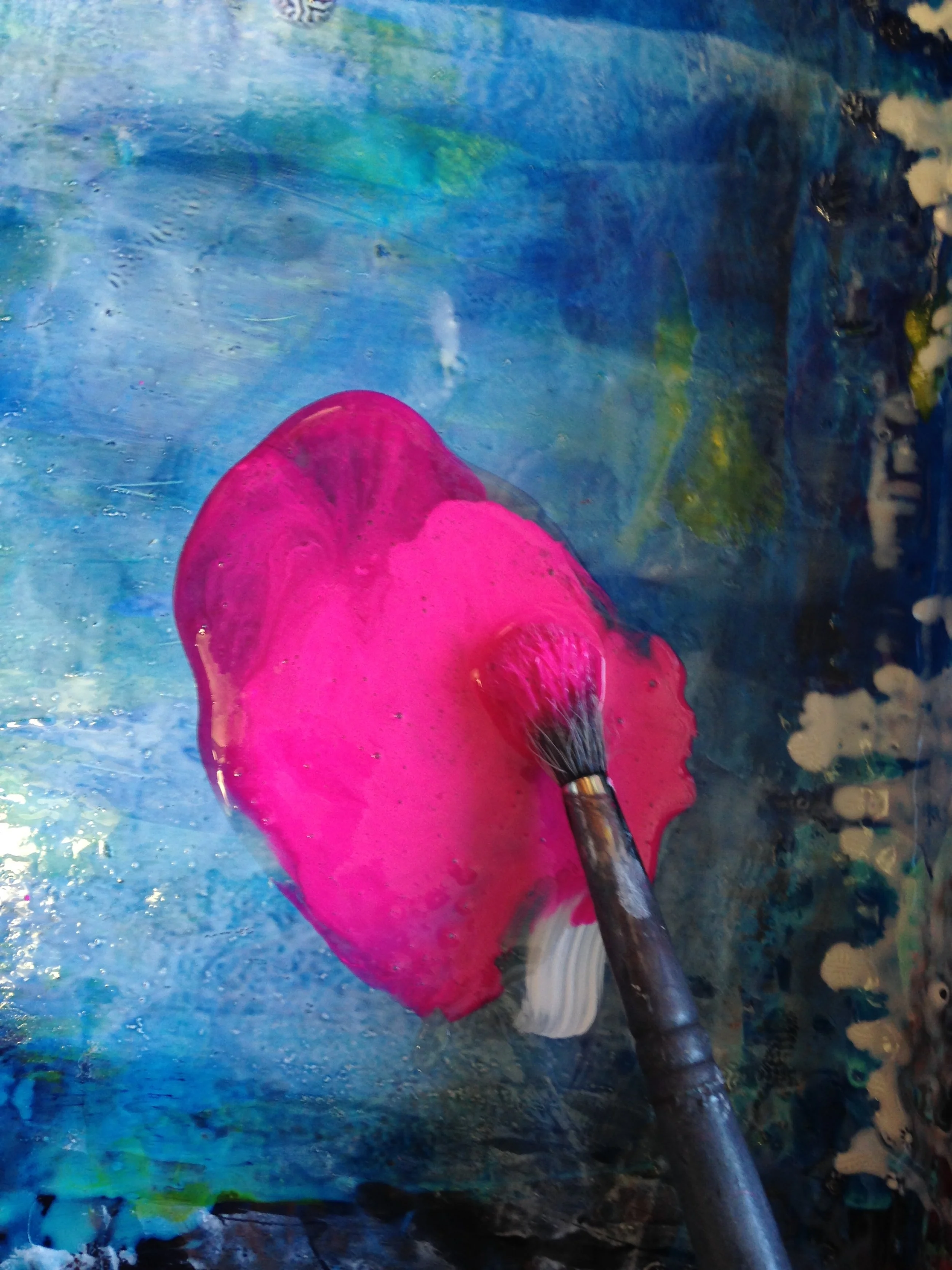 a pool of bright pink paint blended with a medium being mixed with a paint brush on a bright blue tray