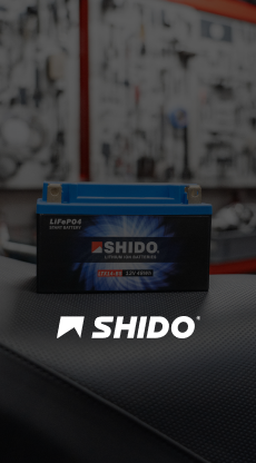 Gros plan d'une batterie de moto Shido bleue sur le tableau de bord d'une voiture avec un arrière-plan flou de garage.
