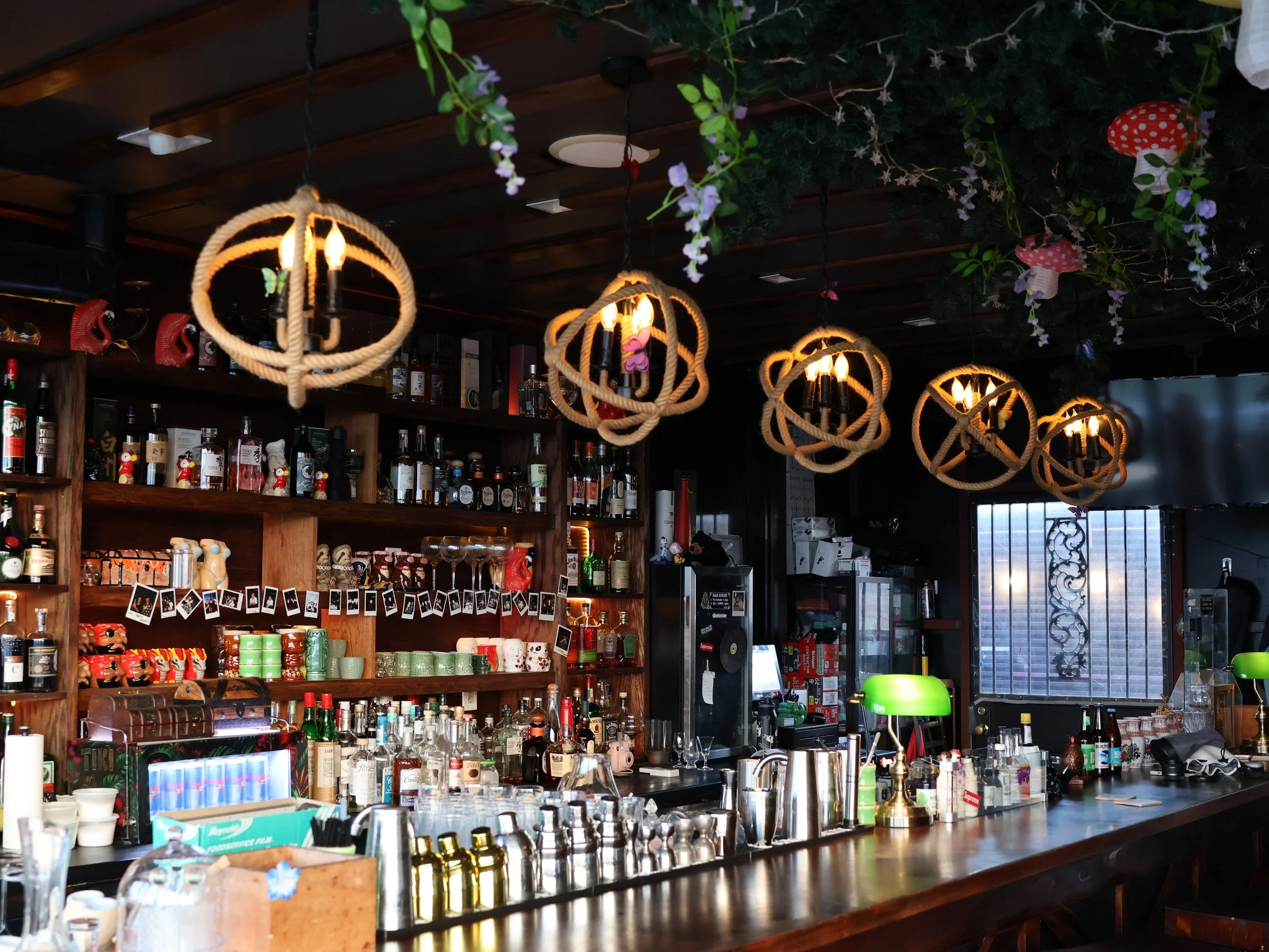 Bar counter with liquor bottles and barware, decorated with hanging rope light fixtures, artificial flowers and hanging mushroom-shaped lanterns.