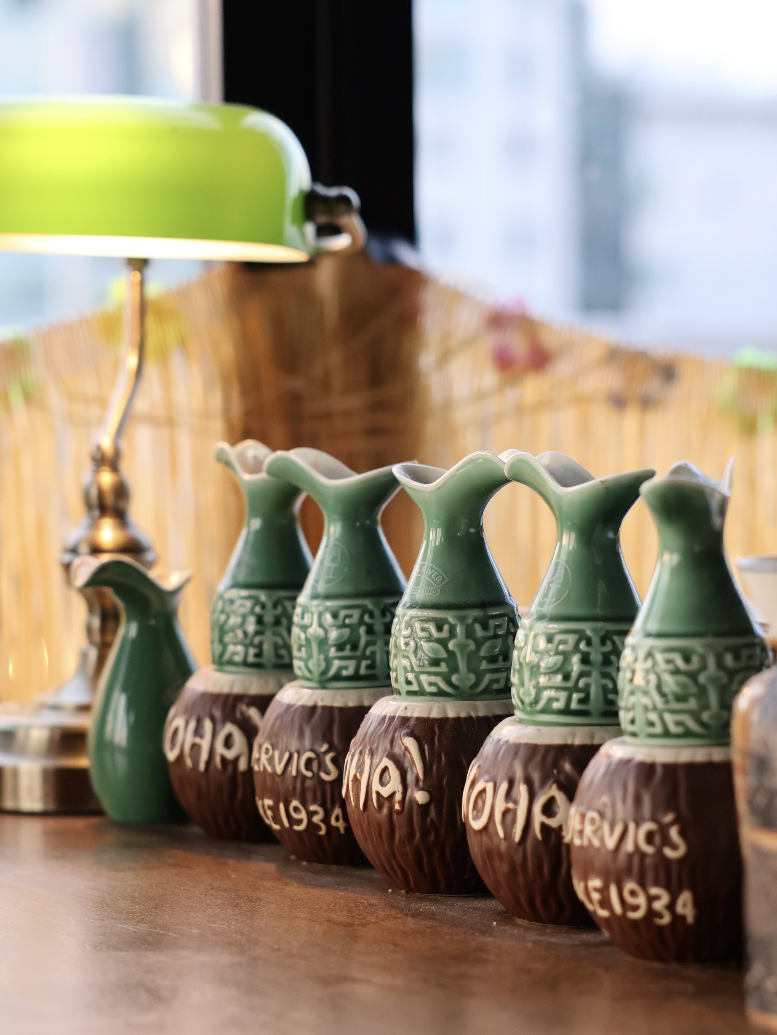 A row of ceramic mugs with green upper parts and brown lower parts, engraved with text, placed on a wooden surface.