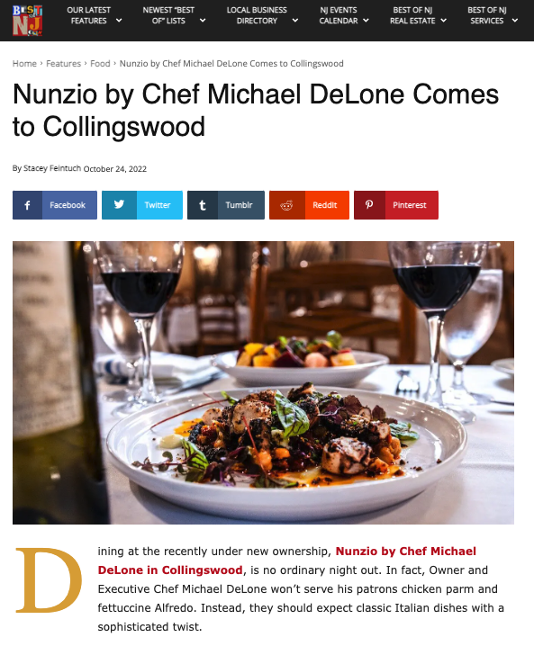 A plated Italian dish with grilled meat, vegetables, and herbs on a white plate, set on a table with two glasses of red wine and a side dish in a restaurant setting.