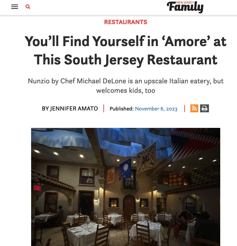 Interior of a restaurant with white tablecloths, wooden chairs, decorative banners hanging from the ceiling, arched doorways, and people dining.