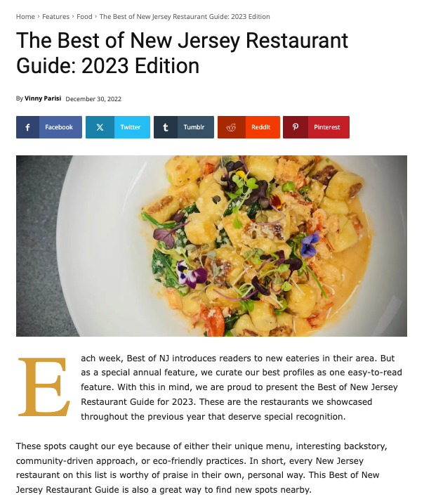A white plate with a serving of gnocchi pasta garnished with microgreens and edible flowers, accompanied by a few pieces of diced vegetables.