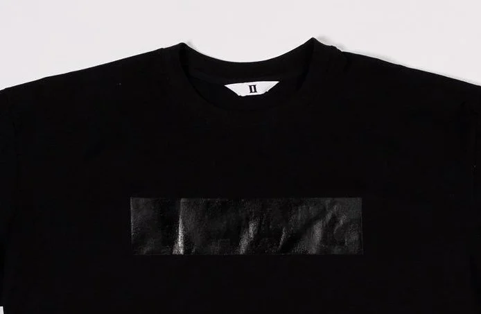 Close up of black t-shirt with gloss black rectangular print on chest, concealing subtle text underneath