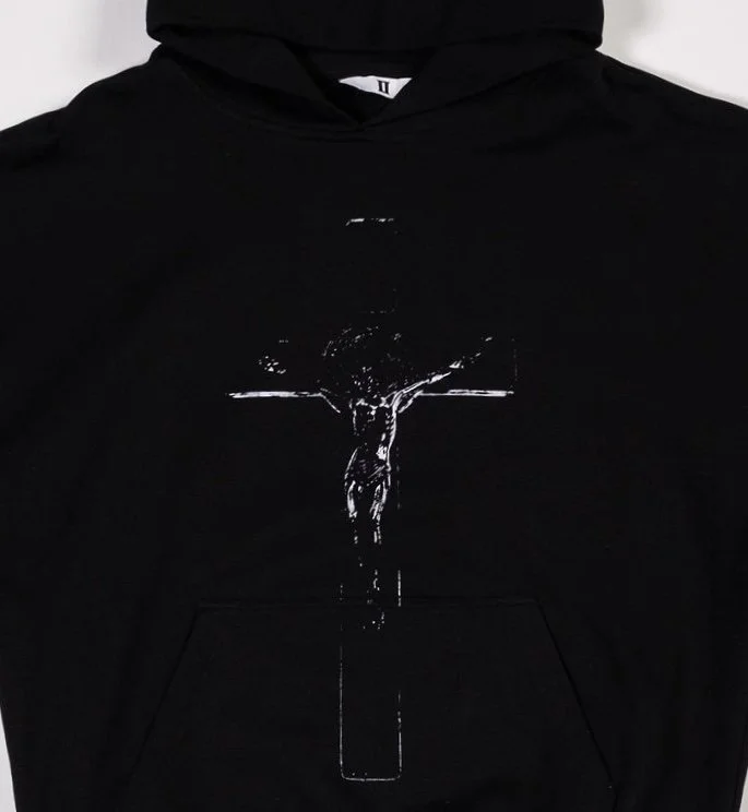 Close up of black pullover hoodie with metallic chrome crucifix outline graphic on the front