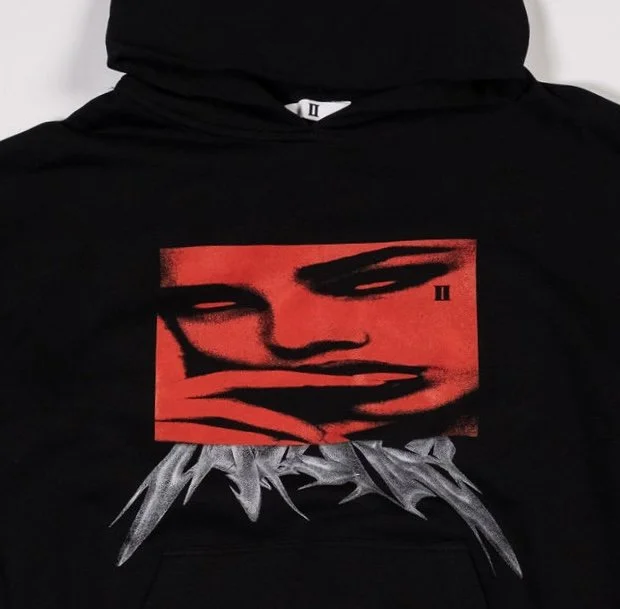 Close up of black pullover hoodie with red graphic of woman’s face and silver metal-style ‘Mirrors’ abstract lettering across chest